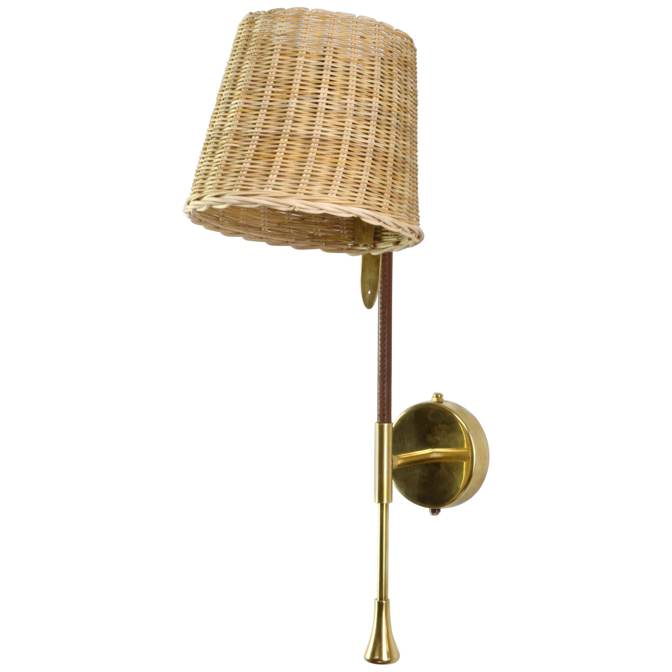 Our bestseller, the Ancora-W2, is a handcrafted articulating wall light fixture composed of a solid brass structure adorned with a sheathed leather detail hand-sewn by artisan saddle workers. The handwoven rattan shade has a 90° rotation and is