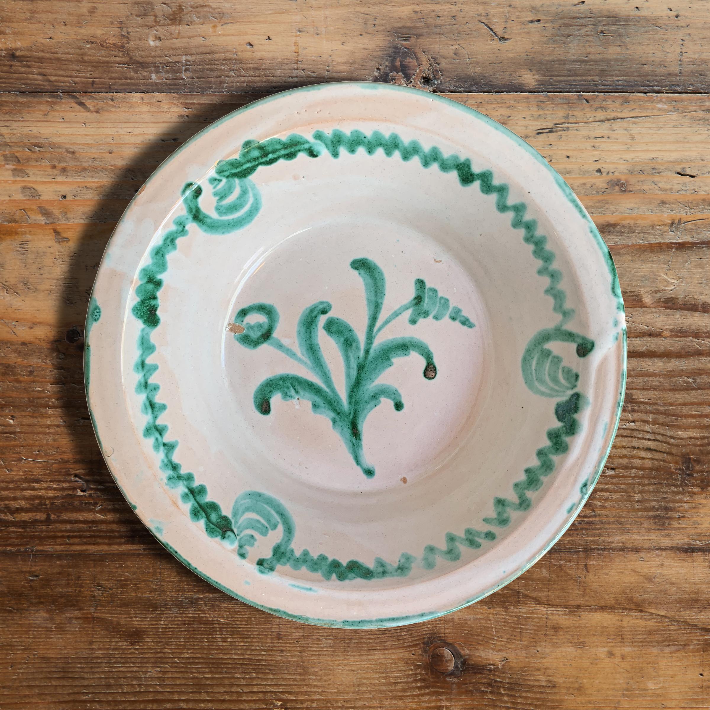 A fantastic Andalusian Talavera pottery bowl with an opaque white glaze and a green glazed decorative pattern and a flower on the bottom.