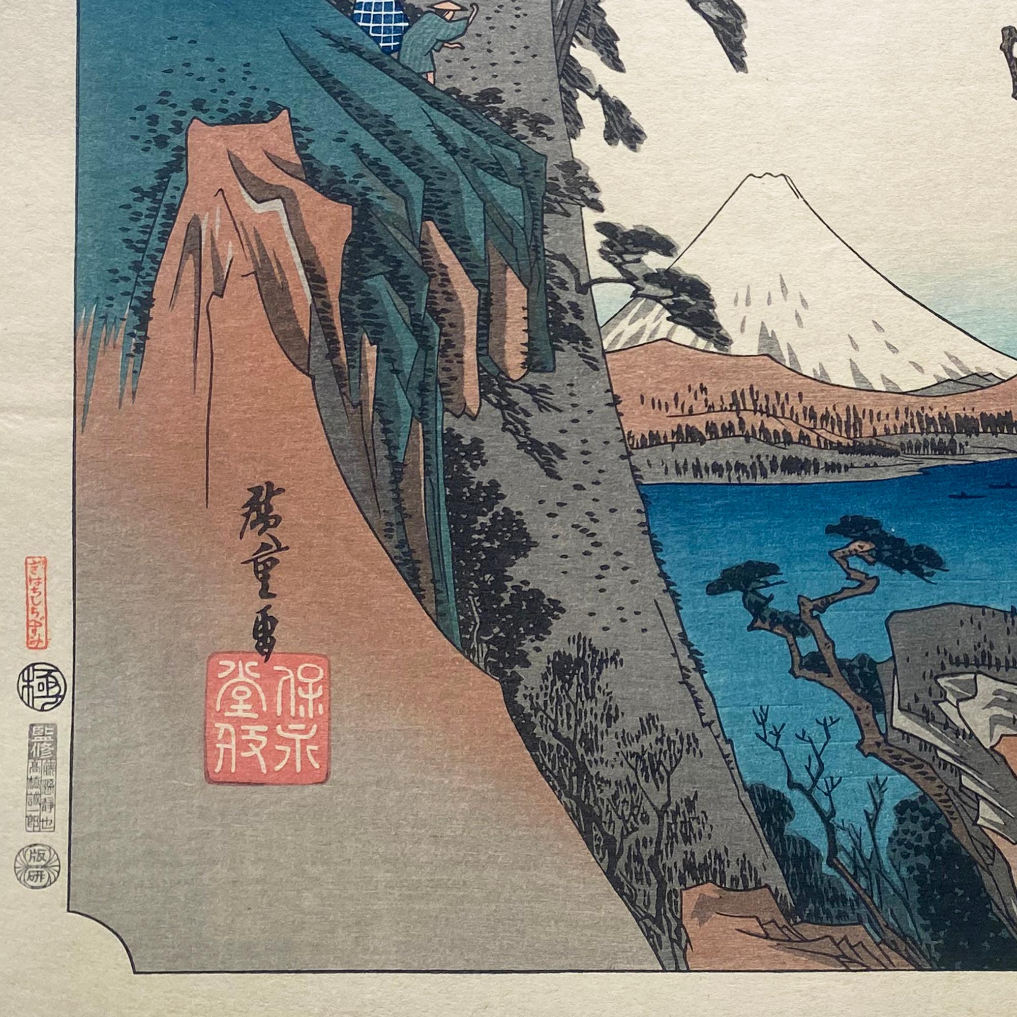 Eine Tusche auf Papier, Nishiki-e- und Yoko-e-Holzschnitt-Landschaft, die Reisende zeigt, die eine Pause von ihrer Wanderung machen, um den Blick auf die Kiyomi-Bucht und den schneebedeckten Berg Fuji zu genießen. Signiert in Kanji unten links,