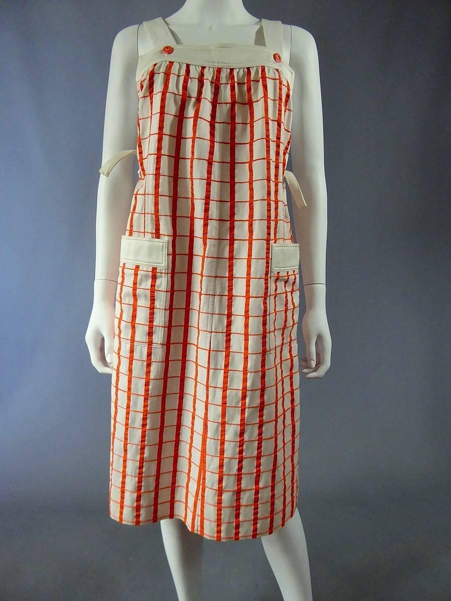 Circa 1970-1980

France

A line shape Haute Couture dress by André Courrèges. Model numbered 19055. Attached with two white straps hold by orange buttons on the face and the back.

Pattern of the dress is checkered with orange lines on white