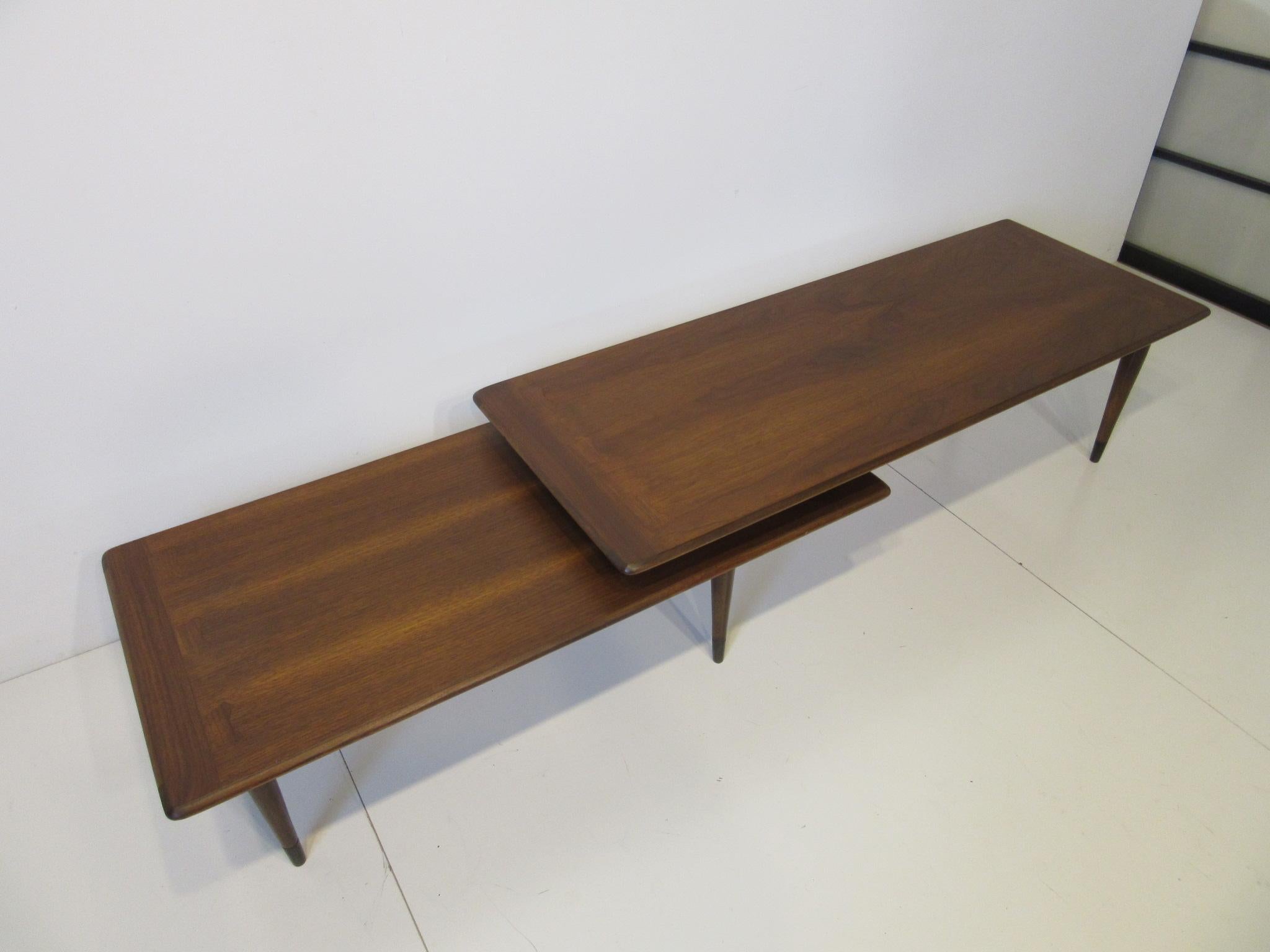 A dark walnut toned switchblade coffee table with pivoting top able to make a L angle, longer size or can be tucked into each other for a shorter length. One of the best designs for versatile living with detail dovetails to the top edges