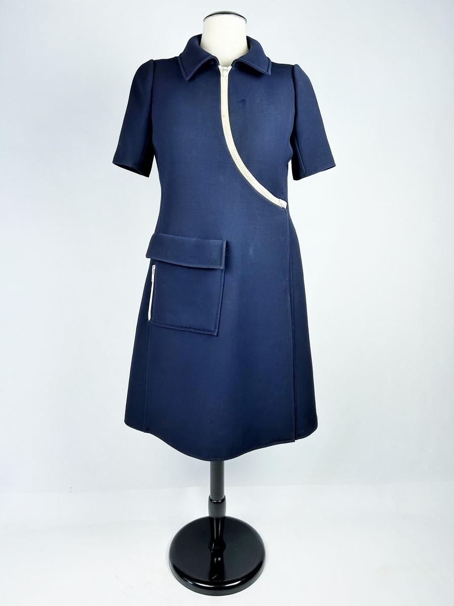 Circa 1970

France

Haute couture wrap dress number 85726 (?) in thick navy blue jersey dating from the 1970s. Flared dress in a chasuble cut with topstitching, short sleeves and a Claudine collar with folded panels. Asymmetrical double-breasted