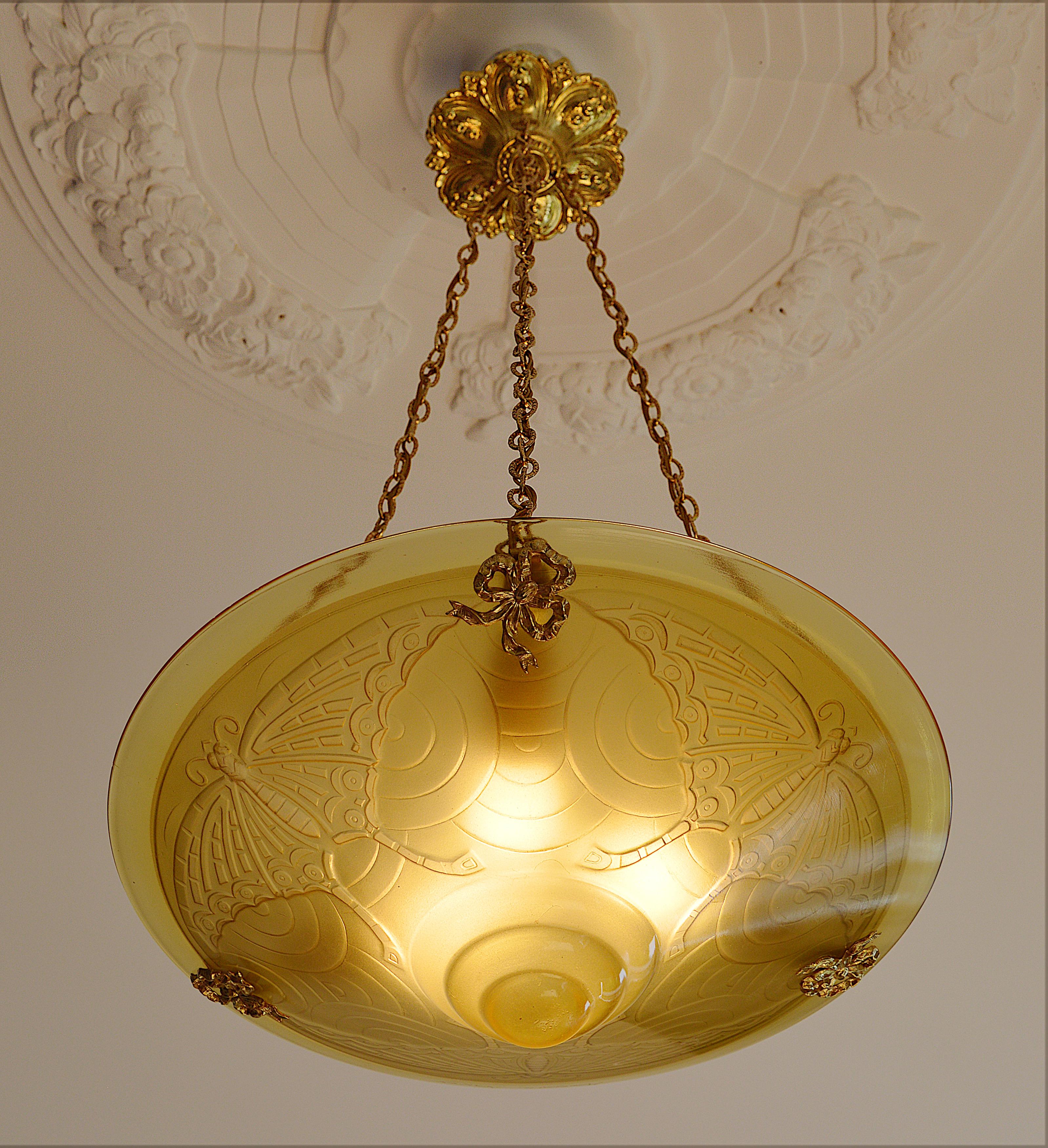 French Art Deco pendant chandelier by André Delatte (Jarville, near Nancy), France, late 1920s. Glass, solid bronze and brass. Molded amber glass shade with a tree butterflies pattern. Brass (canopy and chains) and solid bronze (hidden-holes)