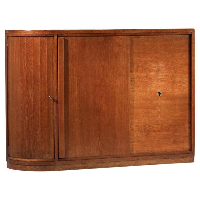1930s sideboard by French designer André Sornay. Structure in solid oak and veneer, highlighted by a system of perfectly aligned brass nails running all around the unit (see photos), a typical André Sornay technique. The sliding door and rounded