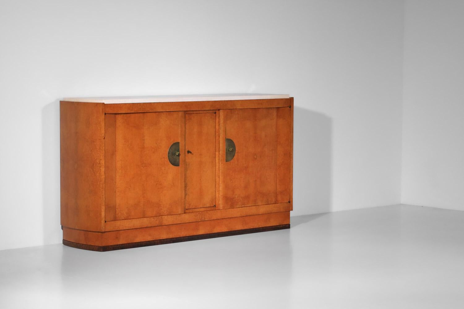 Credenza Art Deco degli anni '30 del secolo scorso del designer francese André Sornay. Struttura in legno impiallacciato e piano in pietra beige. Il mobile presenta tre ante a battente che si aprono su ripiani; le tre chiavi sono incluse nella