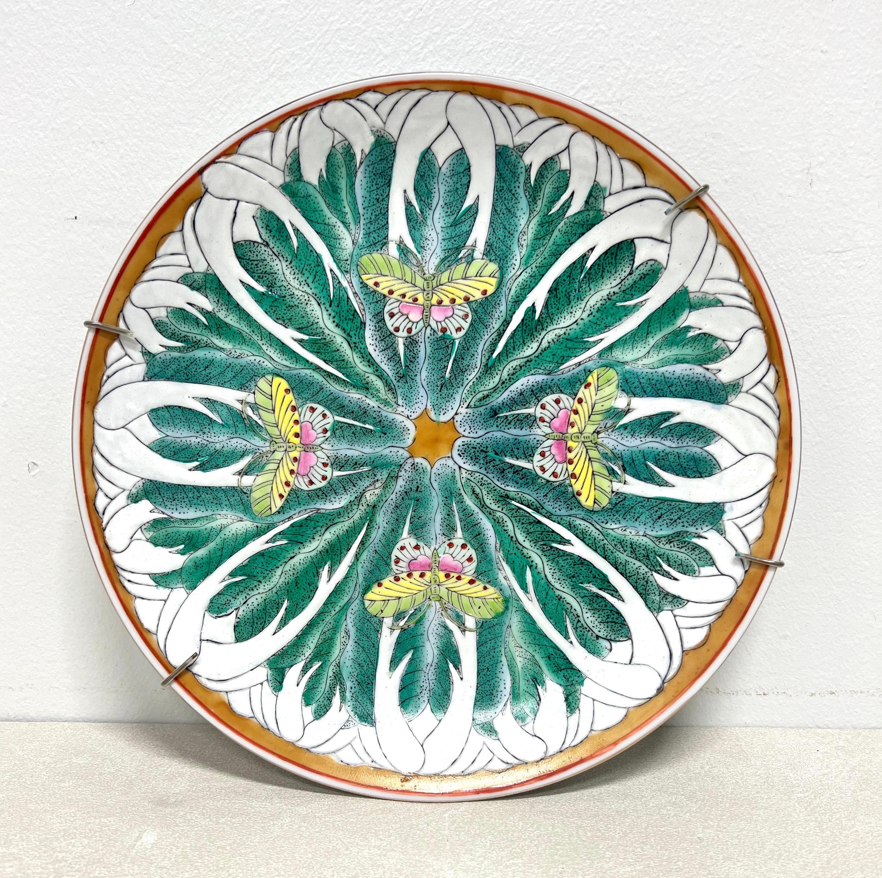 An Asian Chinoiserie style decorative plate by Andrea by Sadek. Hand painted famille vert porcelain with vivid colors, primarily greens, depicting bok choy & butterflies, and gold trim. Comes with a wire wall hanger. Made in China, in the late 20th