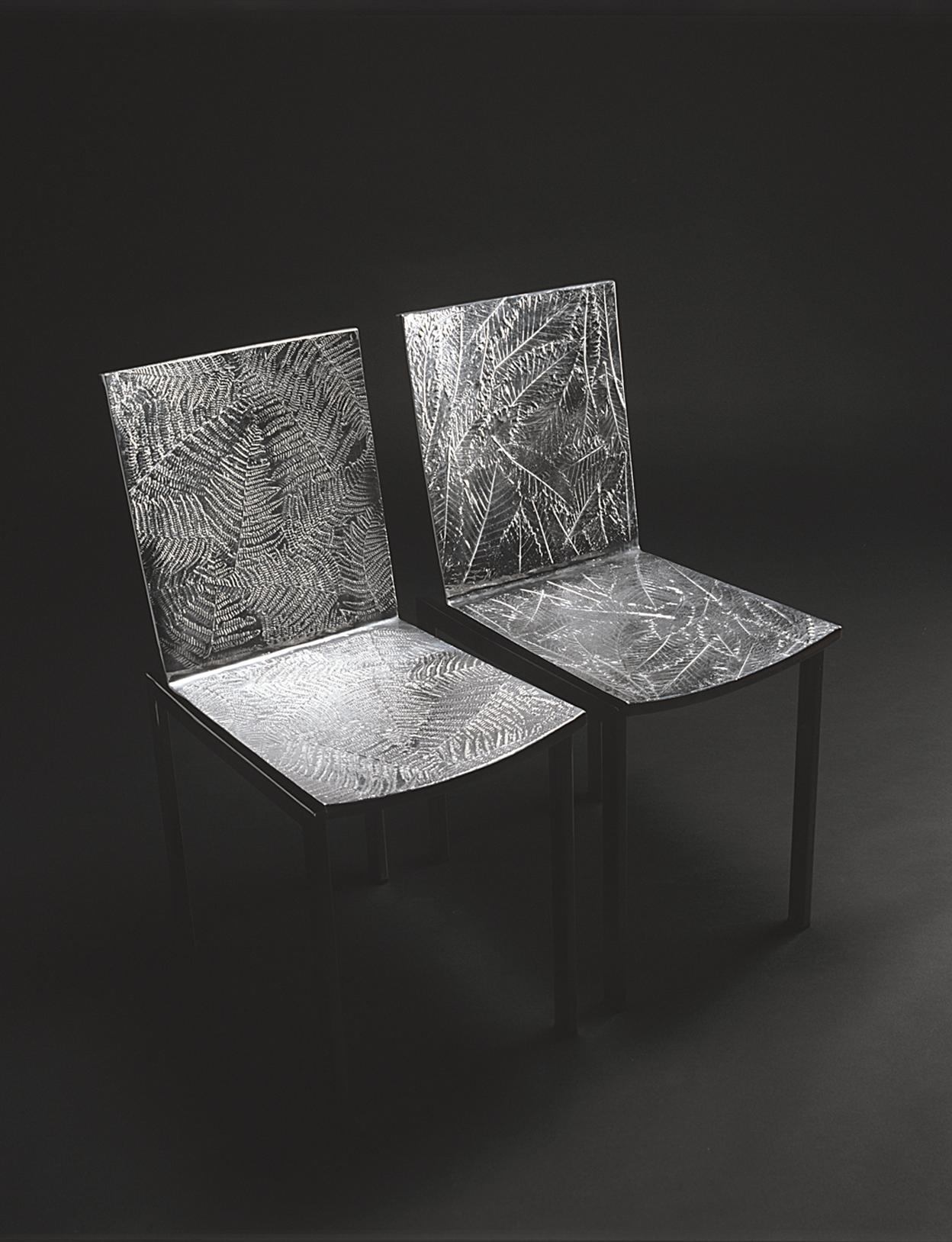 Chaise de salle à manger avec assise en fonte d'aluminium et structure en acier inoxydable brillant. La surface texturée est créée par des panneaux réalisés en moulage d'aluminium avec quatre textures de feuilles différentes : feuille de