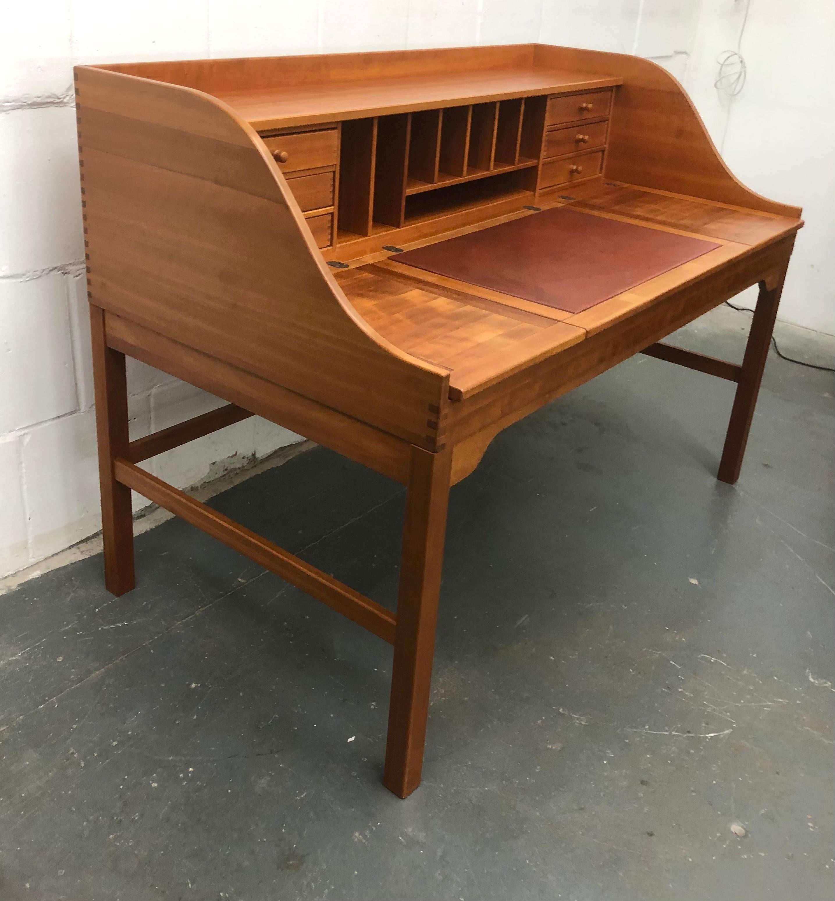 Handsome, masculine cherry wood desk with brass hardware by Andreas Hansen. Nice craftsmanship with beautiful dovetail construction, 6 small drawers and storage areas, 3 flip-up panels with storage beneath, and deep red leather writing blotter. The