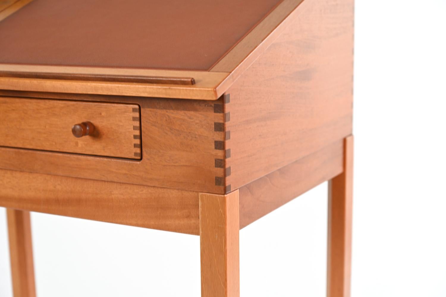 A Danish mid-century tall free-standing desk in blonde cherry wood with beautiful exposed dovetail joints. Featuring a brick red leather flip up top, single drawer, and fitted interior. With Form 75 Danish label underneath. Designed by Andreas