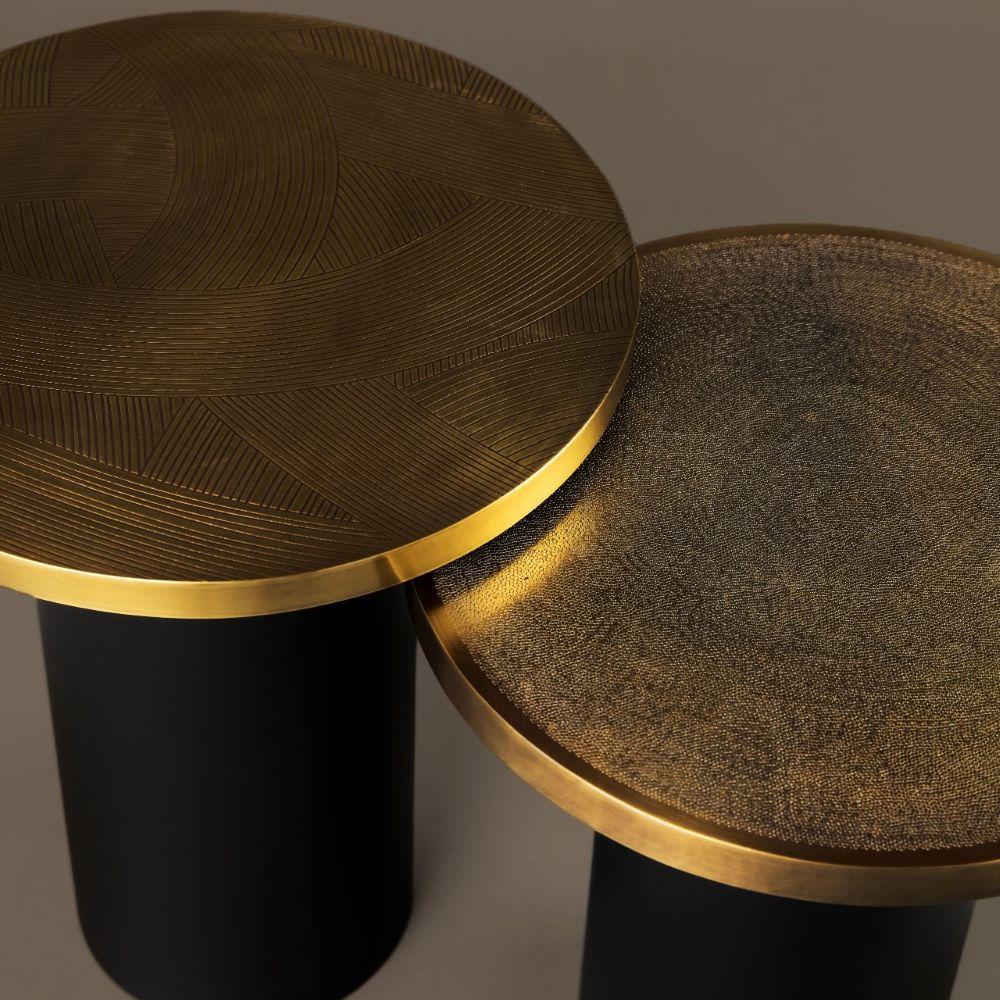Cette paire de tables d'appoint allie l'élégance du laiton travaillé à la main à la présence discrète d'une base cylindrique en acier noir. Chaque table est définie par la texture unique de son plateau et ses proportions distinctes.

Le modèle