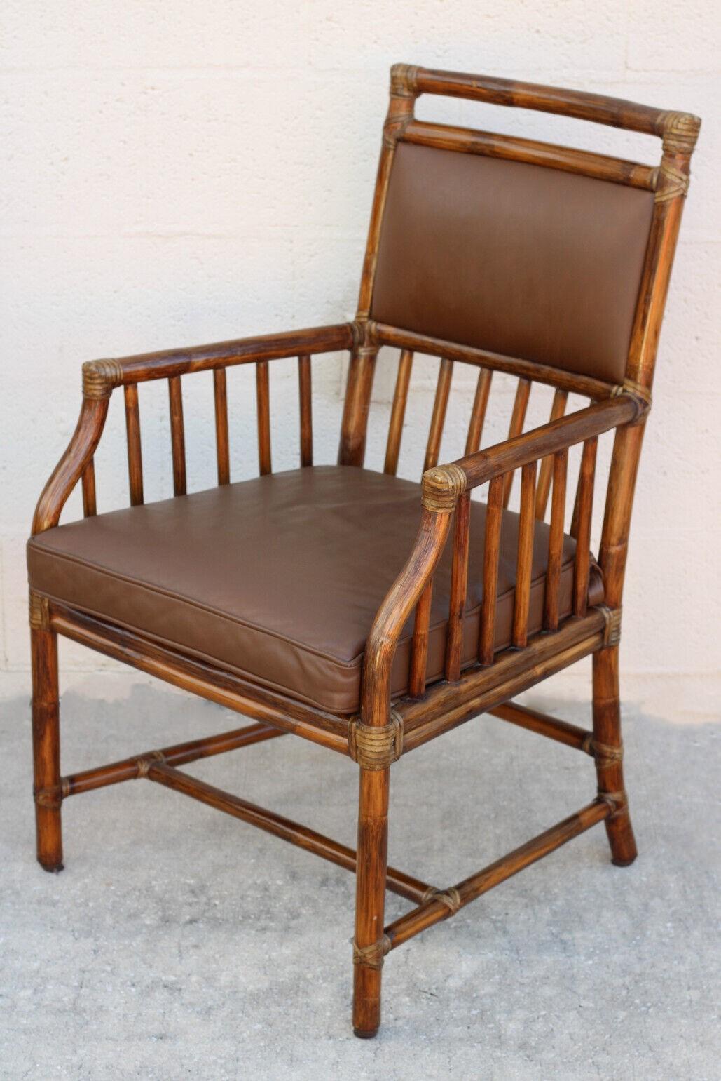 A pair of vintage McGuire rattan and leather arm chairs or dining chairs, featuring Craftsman details. The chairs were designed by Andrew Delfino and have a rich dark tobacco finish along with supple leather seat backs and leather cushions placed