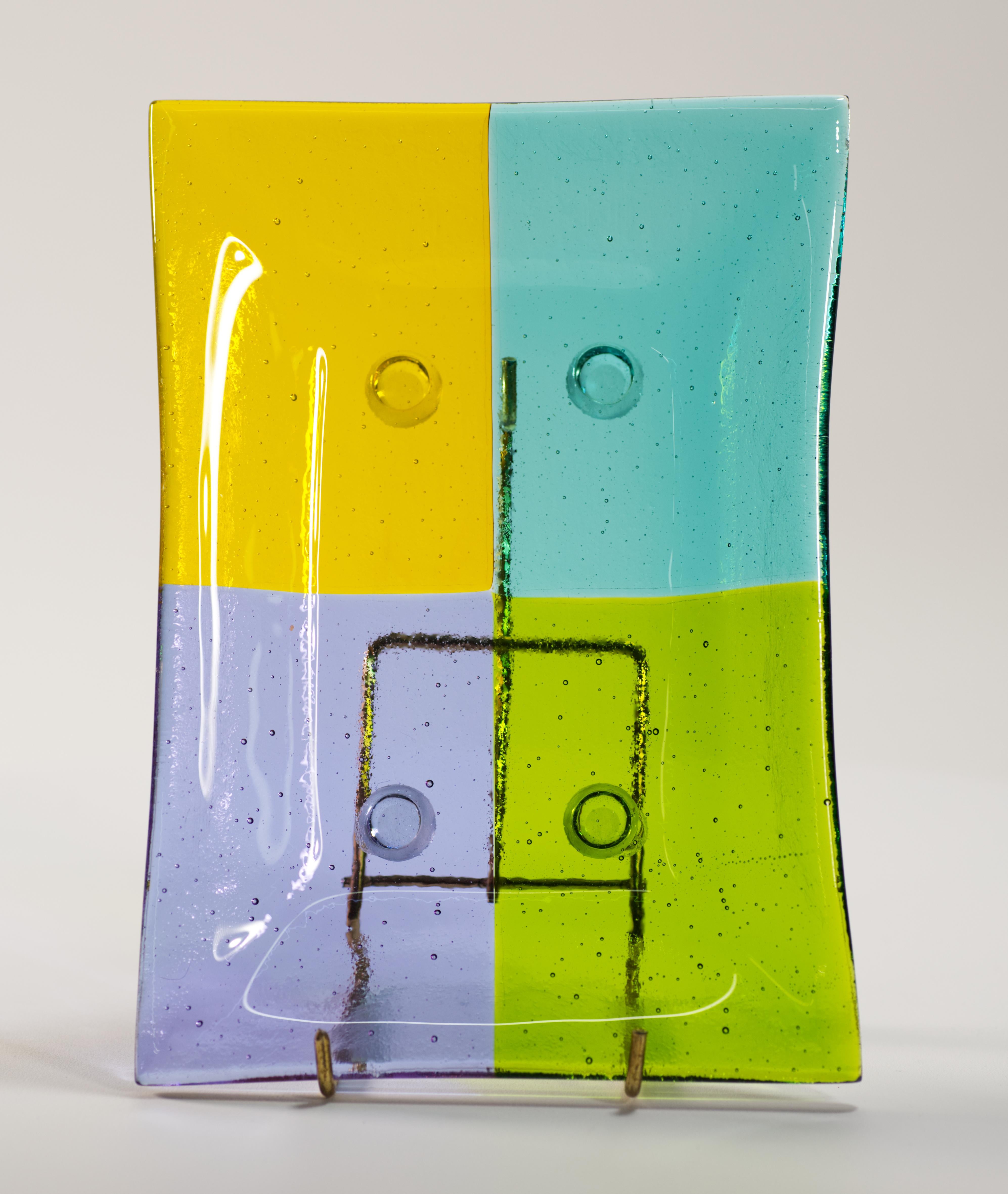  Il vassoio con piede in vetro artistico vintage presenta un colorato design in vetro fuso Op-art con elementi in vetro colorato viola, giallo marigold, verde bosco e blu acqua fusi senza soluzione di continuità in un vassoio rettangolare. Il