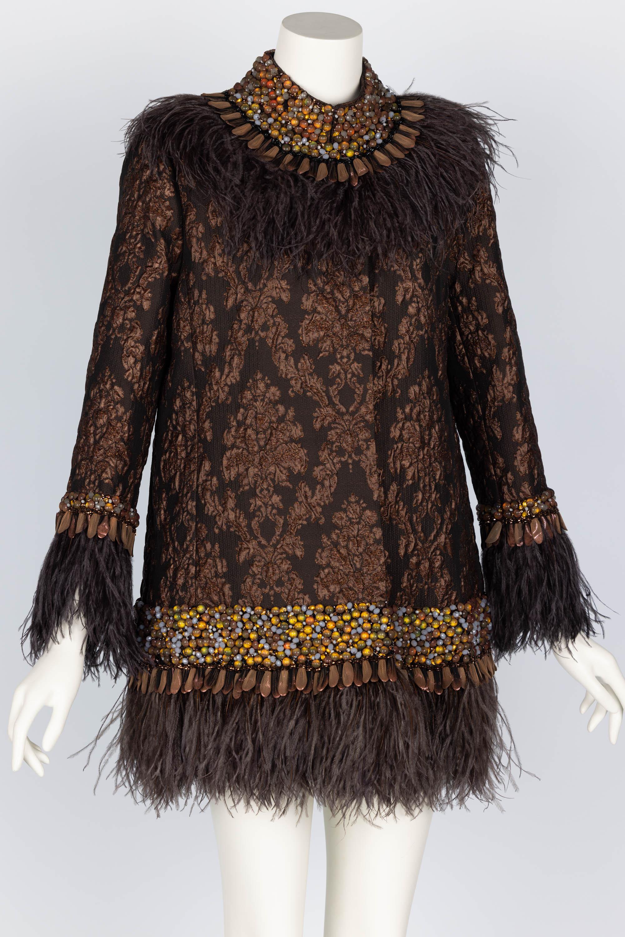 Done in a rich brown silk brocade with metallic copper accents. A collage of jewels covered in tulle surrounds the collar, cuff, and bottom of this evening coat. Brown feather trim. 
Fully lined.
Concealed snap closures.
Excellent condition.

Size