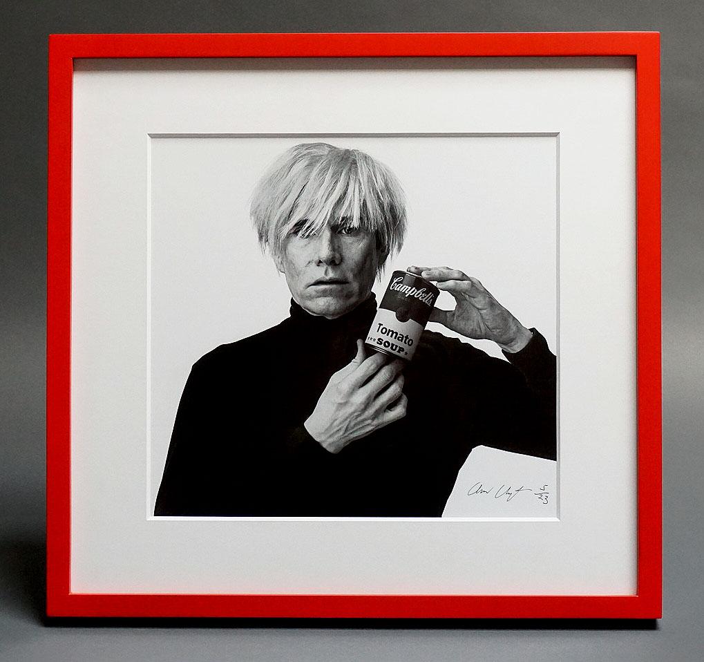 Andrew Unangst's portrait of Pop Artist Andy Warhol, taken in 1985 at Unangst's studio in New York City, captures Warhol at his most iconic: wearing his signature black turtle-neck and white wig, and holding a can of Campbell's tomato soup. The red