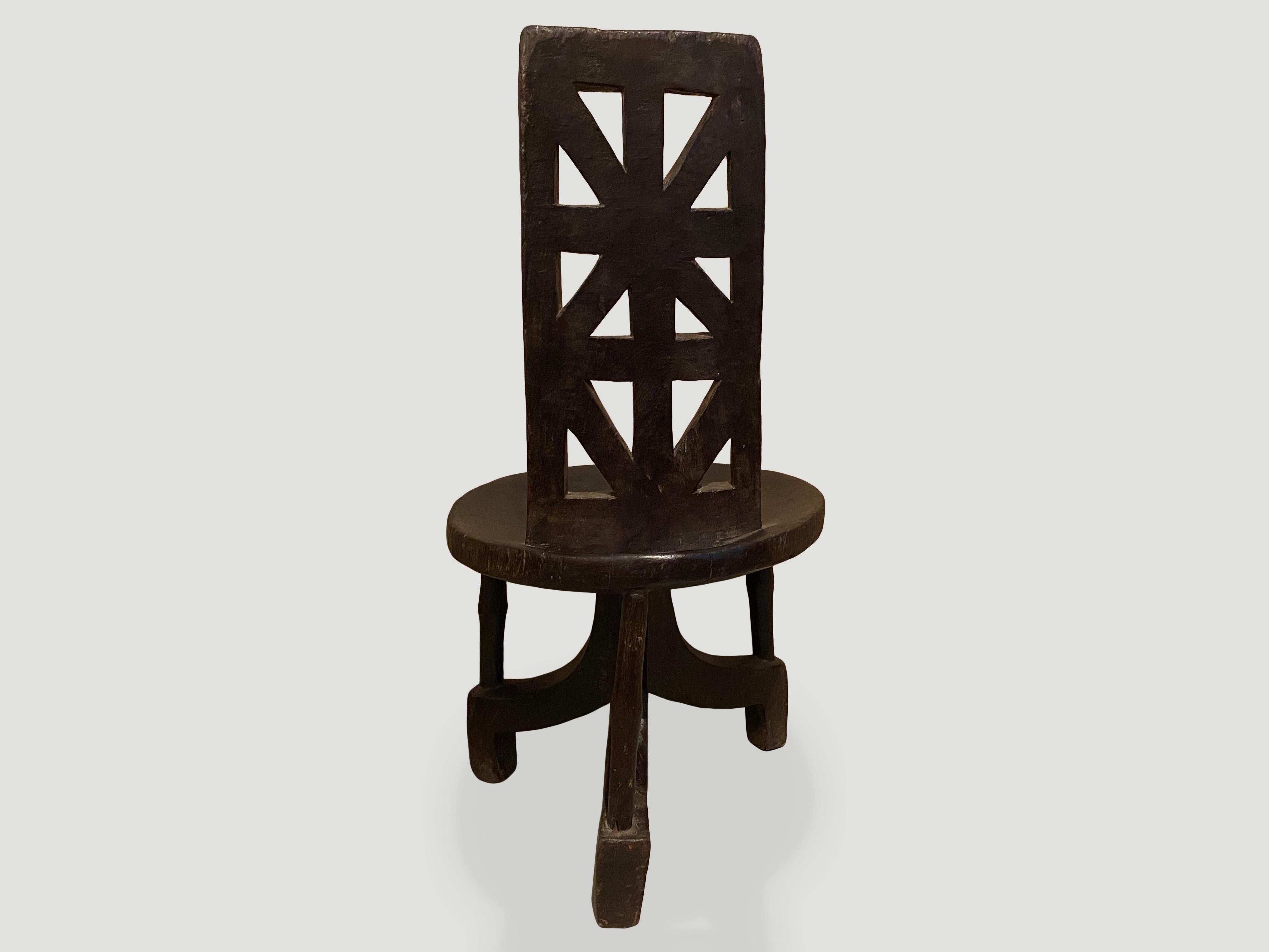 This hand carved wooden chair is from the Jima people of Southern Ethiopia. A slightly concave seat sits on a tripod base connected by slender rods. The high rectangular back rest has a geometric design. Carved out of a single block of wood. Both an