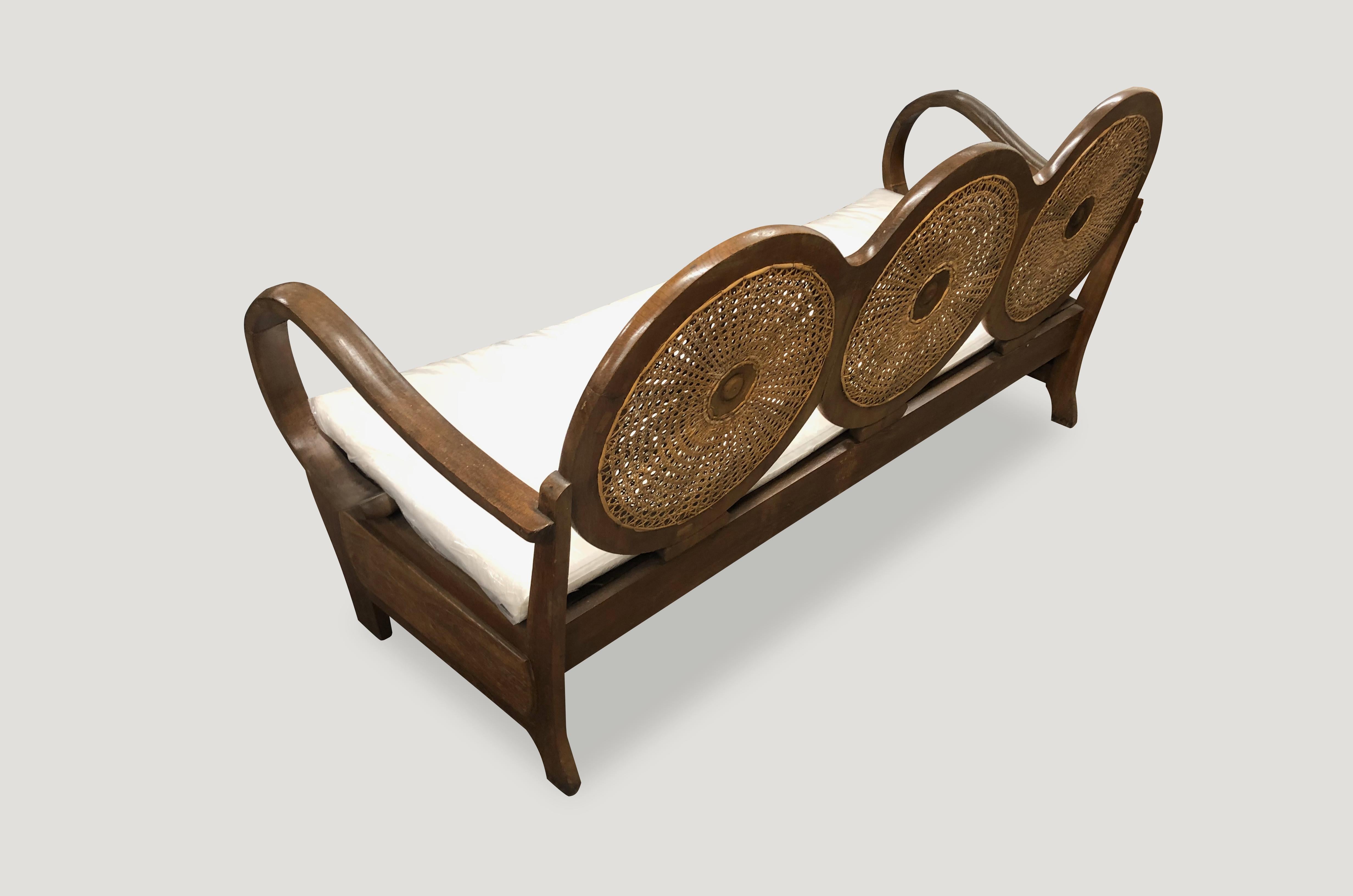 Sofa aus Teakholz mit handgeflochtenem Rattan aus der Mitte des Jahrhunderts. Atemberaubende kreisförmige Rückenlehne und abgerundete Armlehnen, handgeschnitzt aus einem einzigen Stück Teakholz mit schöner Patina. Das Sofa wird mit einem weißen