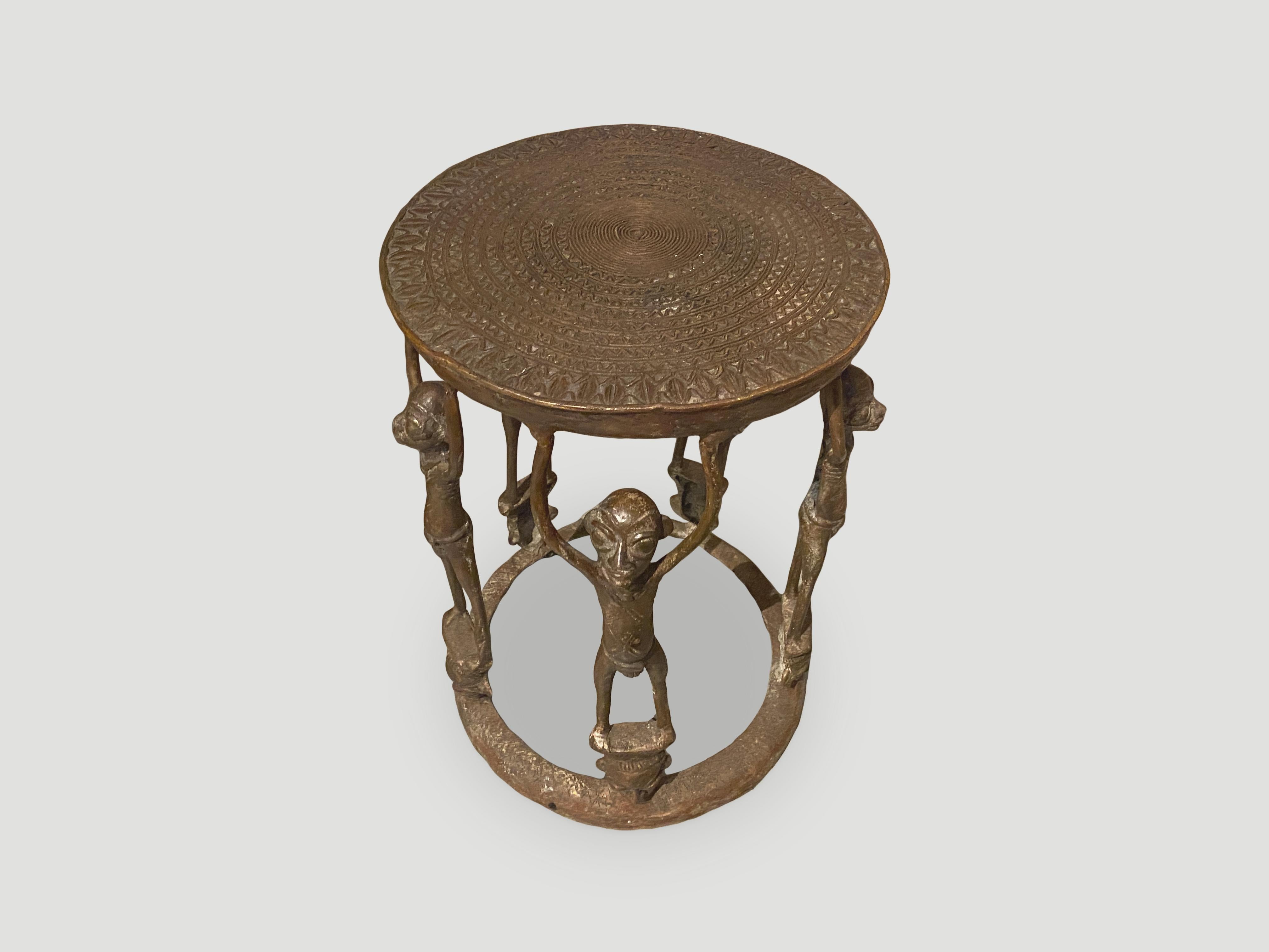 Antique bronze figural side table, from Cameroon. Mid 20th century. Two tiered table with bronze figures resting above masks on the lower level. Whimsical and unique. We only select the best. 

This side table was sourced in the spirit of