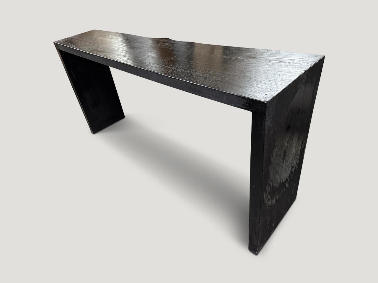 Consola minimalista de madera de teca carbonizada. La parte trasera de la consola está cortada recta para que se apoye en la pared, mientras que la parte delantera tiene un ligero borde vivo Carbonizada, lijada y sellada para revelar la hermosa veta
