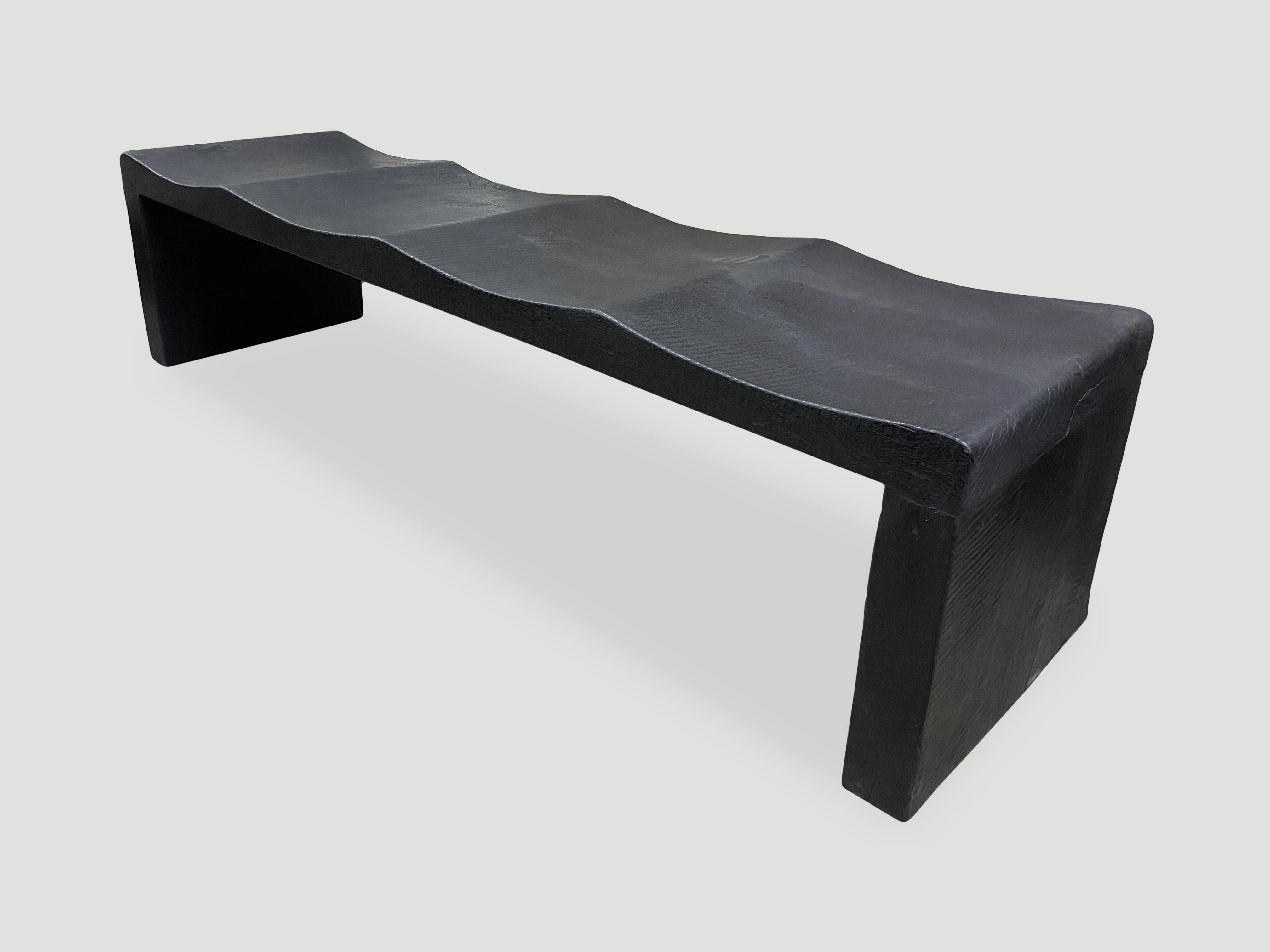 The wave bench represents a sleek, modern aesthetic, designed to provide comfort and durability. Solid reclaimed mango wood is hand carved from a single thick slab into a wave design with added butterfly detail. Burnt, sanded and sealed revealing
