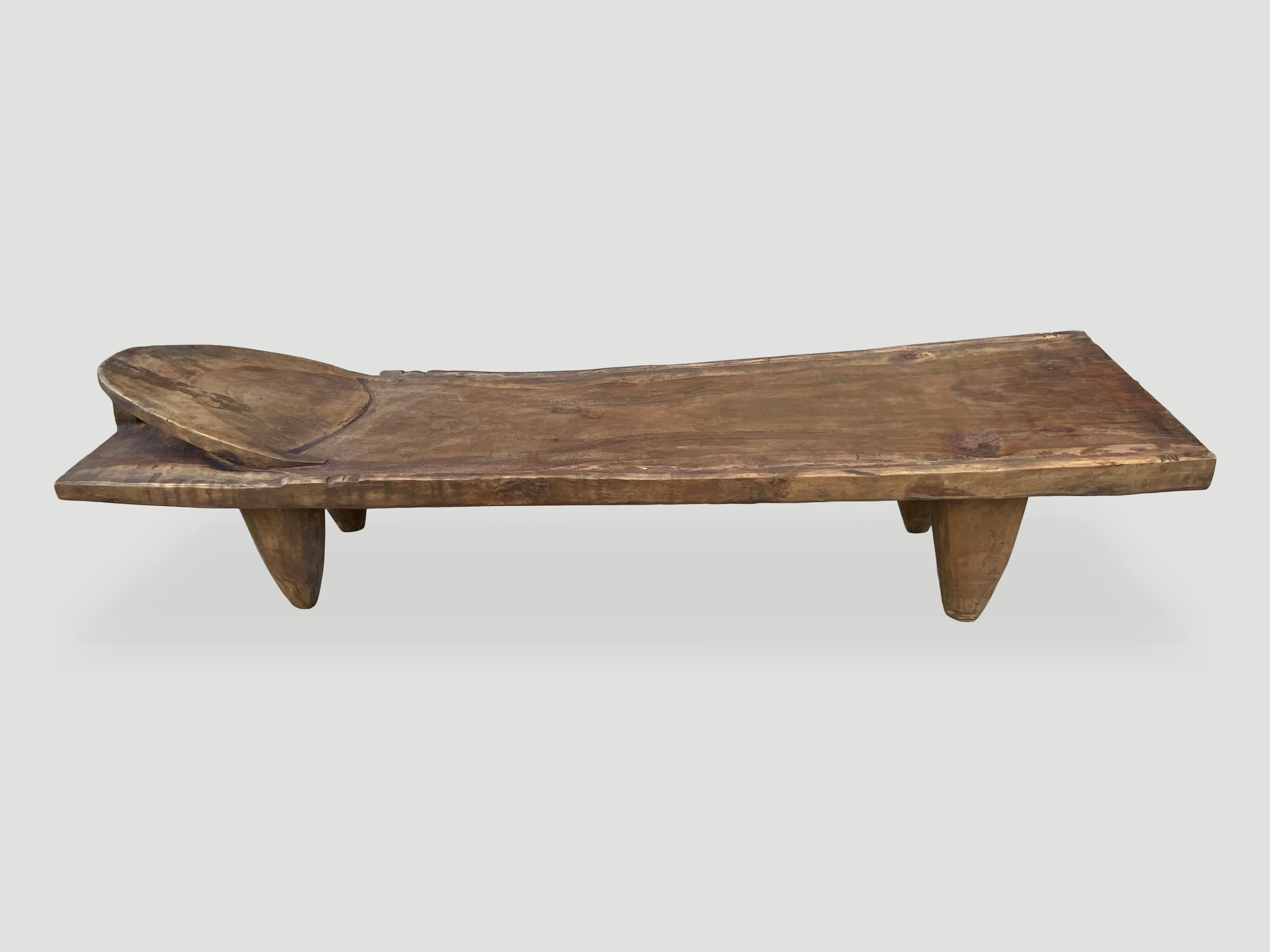 Hand carved by the Senufo tribes from a single block of iroko wood, native to the west coast of Africa. The wood is tough, dense and very durable. Shown with cone style legs and a raised five inch headrest. Originally used as a bed, that can now be
