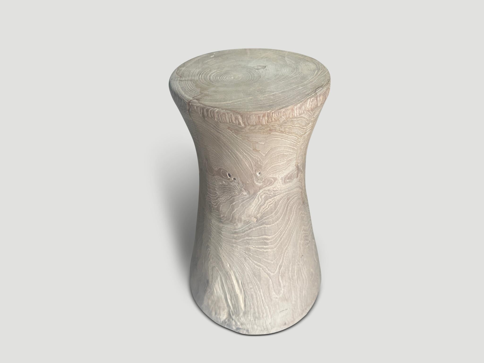 Sculptural hourglass side table or stool. Bleached and then finished with a light white wash revealing the beautiful grain on this century old teak wood. It’s all in the details. Pair available. The price and images reflect the one shown. Full