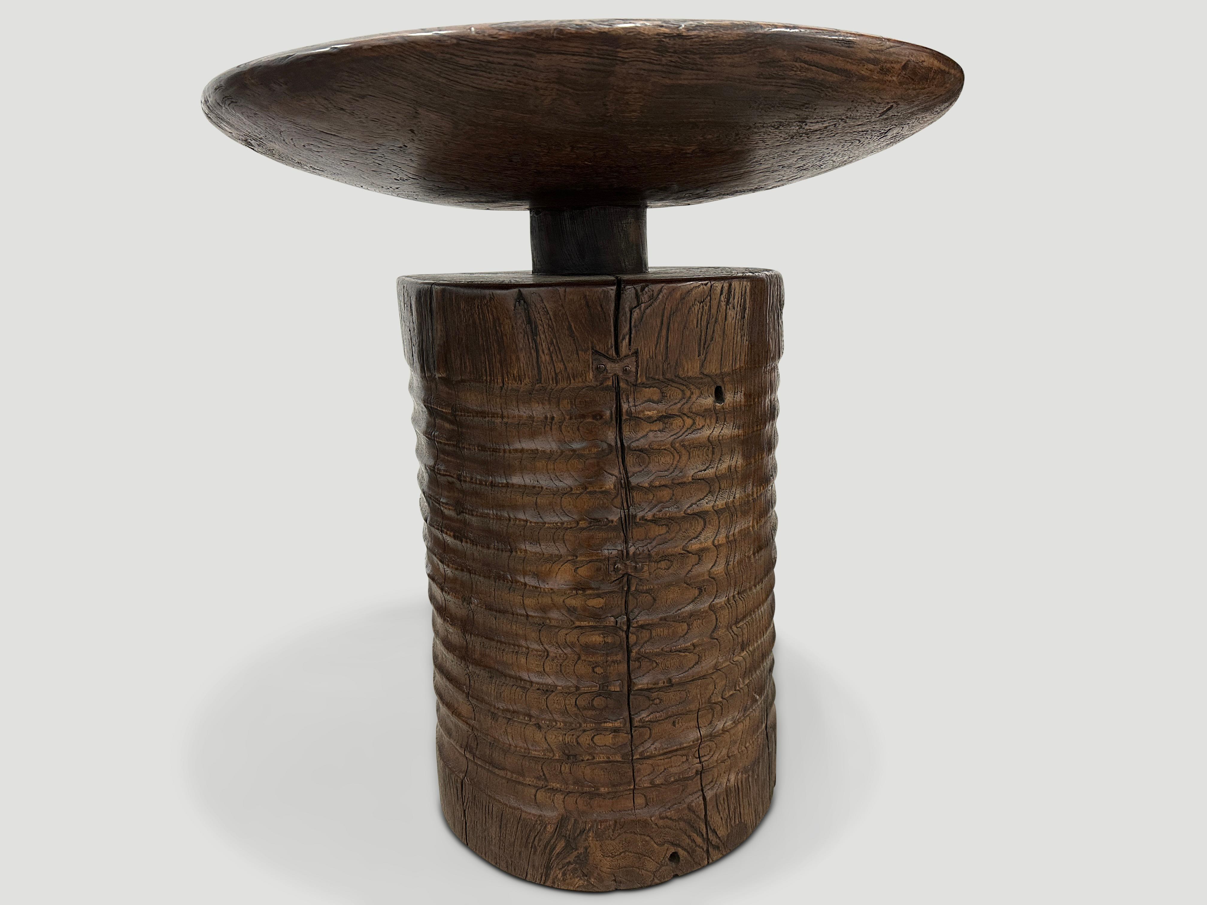 A century old mortar originally used to grind rice is repurposed into this unique side table or entrance table featuring our unique minimalist carving. We added a single teak thick bevelled round top and a translucent chocolate stain revealing the