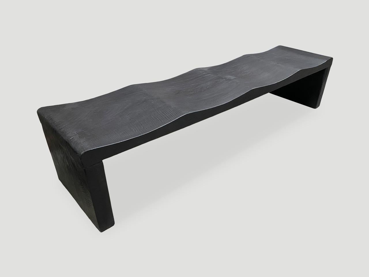 The wave bench represents a sleek, modern aesthetic, designed to provide comfort and durability. Solid reclaimed mango wood is hand carved from a single thick slab into a wave design with added butterfly detail. Burnt, sanded and sealed revealing