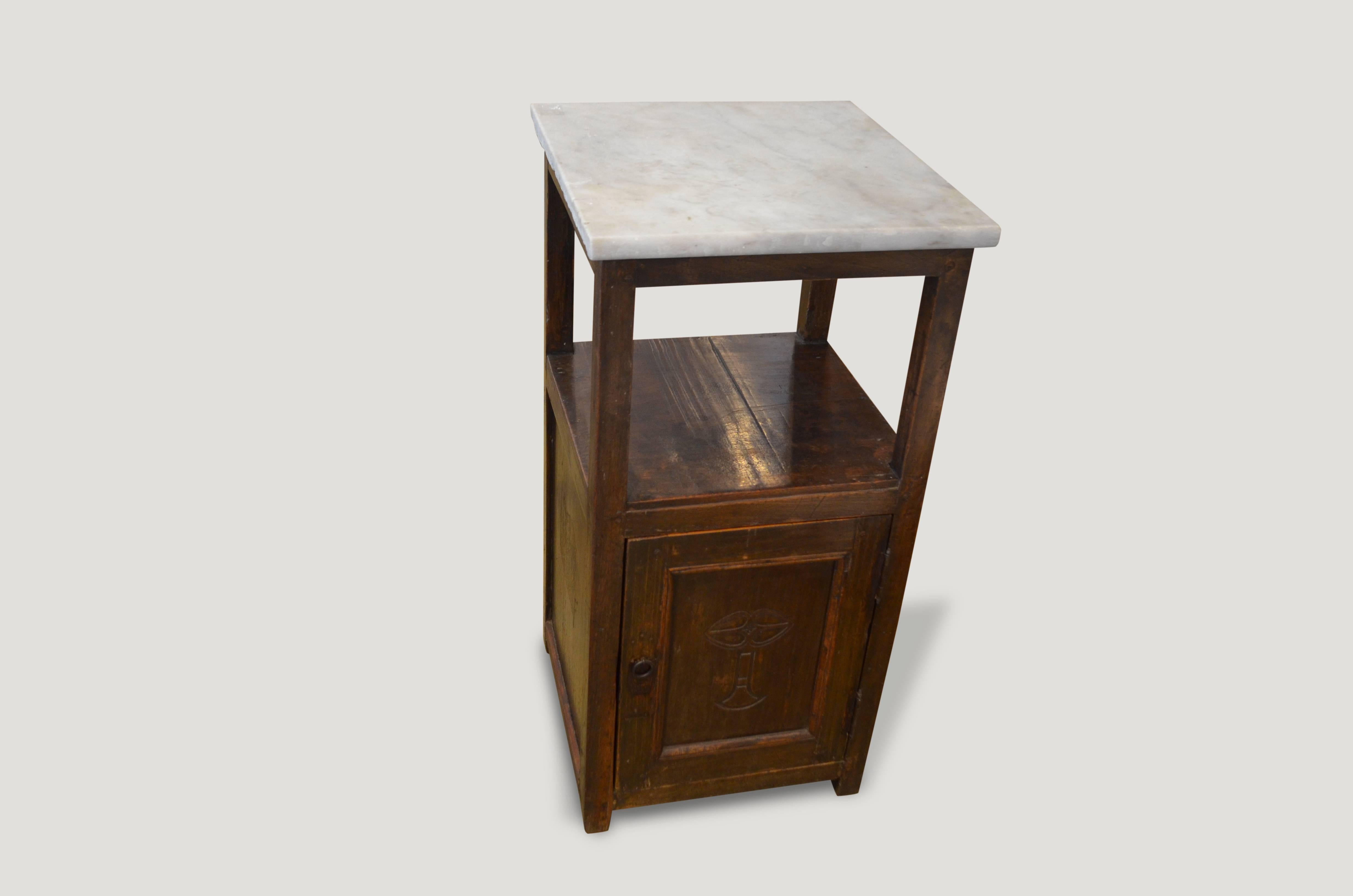 Teak wood side table with a hand carving on the small door section. The top is Italian marble. Original hardware and nice patina.

This side table was sourced in the spirit of wabi-sabi, a Japanese philosophy that beauty can be found in