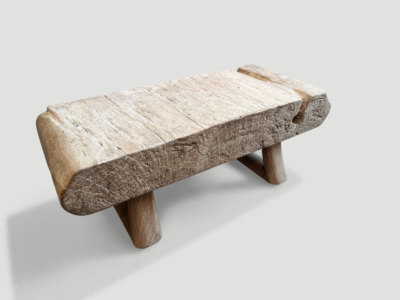 Impressionnante table basse ou banc en bois de teck centenaire avec une volute sculptée à la main à une extrémité. Nous avons ajouté une base triangulaire minimaliste et fini le dessus avec une teinture laiteuse translucide révélant le magnifique
