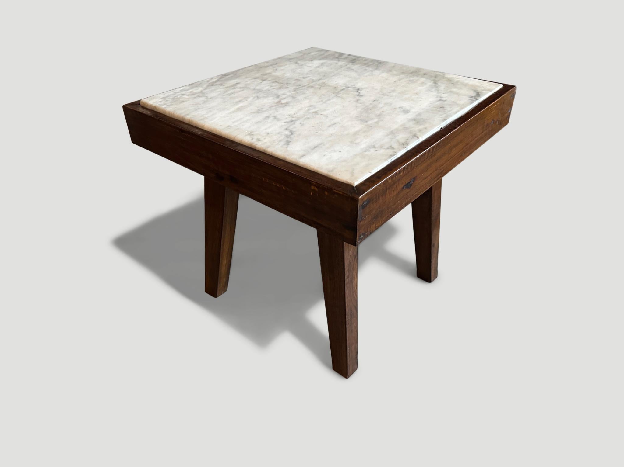A single slab of marble rests inside a teak wood frame. Please note the sides of the marble have a little wear due to the age.

This side table was sourced in the spirit of Wabi-Sabi, a Japanese philosophy that beauty can be found in imperfection