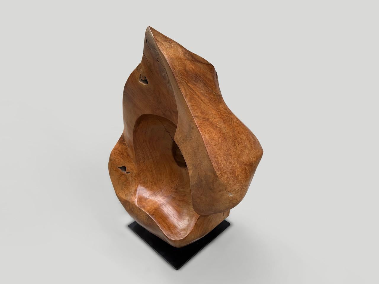 Sculpture minimaliste sculptée à la main dans un seul bloc de bois de teck centenaire. Finition avec une huile naturelle révélant le magnifique grain du bois. Sur un support moderne en métal noir 12