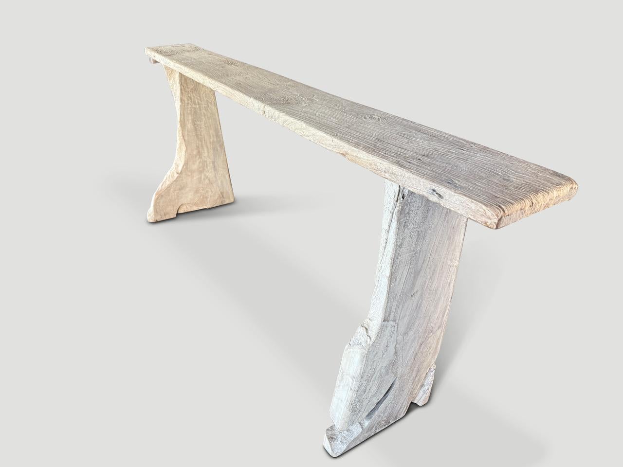 Impressive console table made from a hundred year old reclaimed teak wood. Two solid unique sculptural legs support the thick ancient teak wood panel on top. We added butterfly details and finished with a light white wash revealing the beautiful