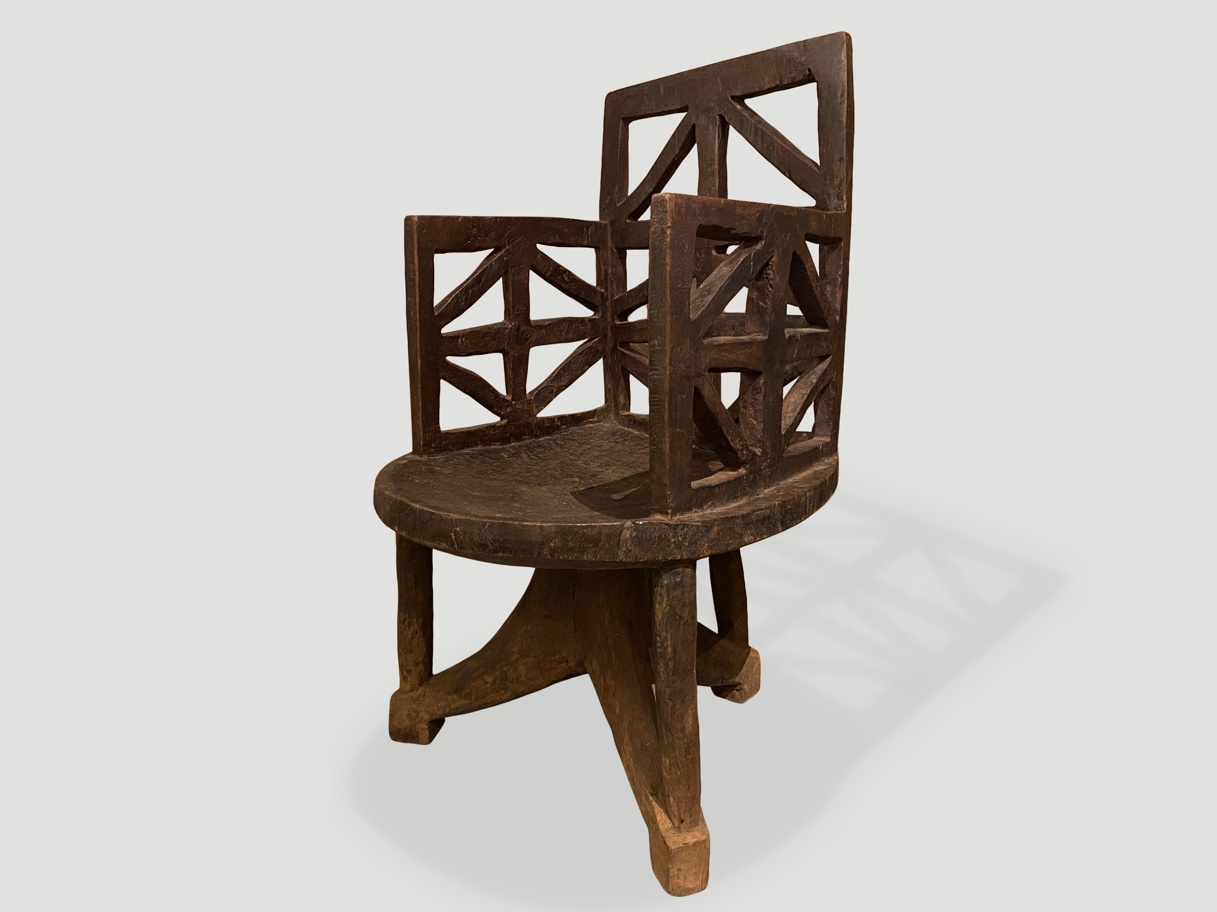 Beautiful hand carved wooden chair from the Western Ethiopian Empire. A slightly concave seat sits on a tripod base connected by slender rods. The high rectangular back rest and arms have a geometric design. Carved out of a single block of wood.