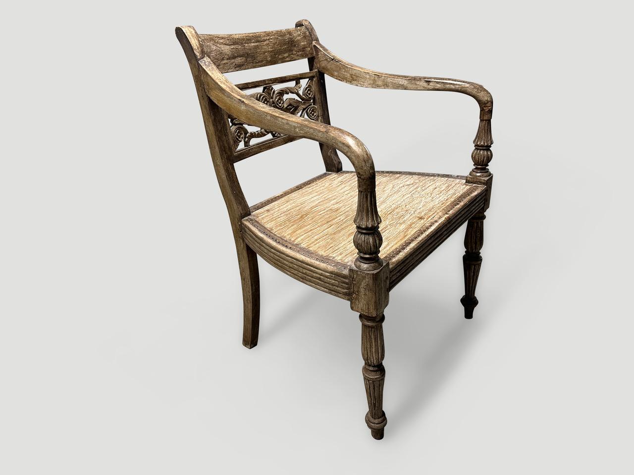 Stunning hand carved teak arm chair with beautiful patina. The front legs and arm rests are beautifully fluted and hand carved. The rattan seat has been replaced with wood. We have a collection of four all one of a kind. The price and images reflect