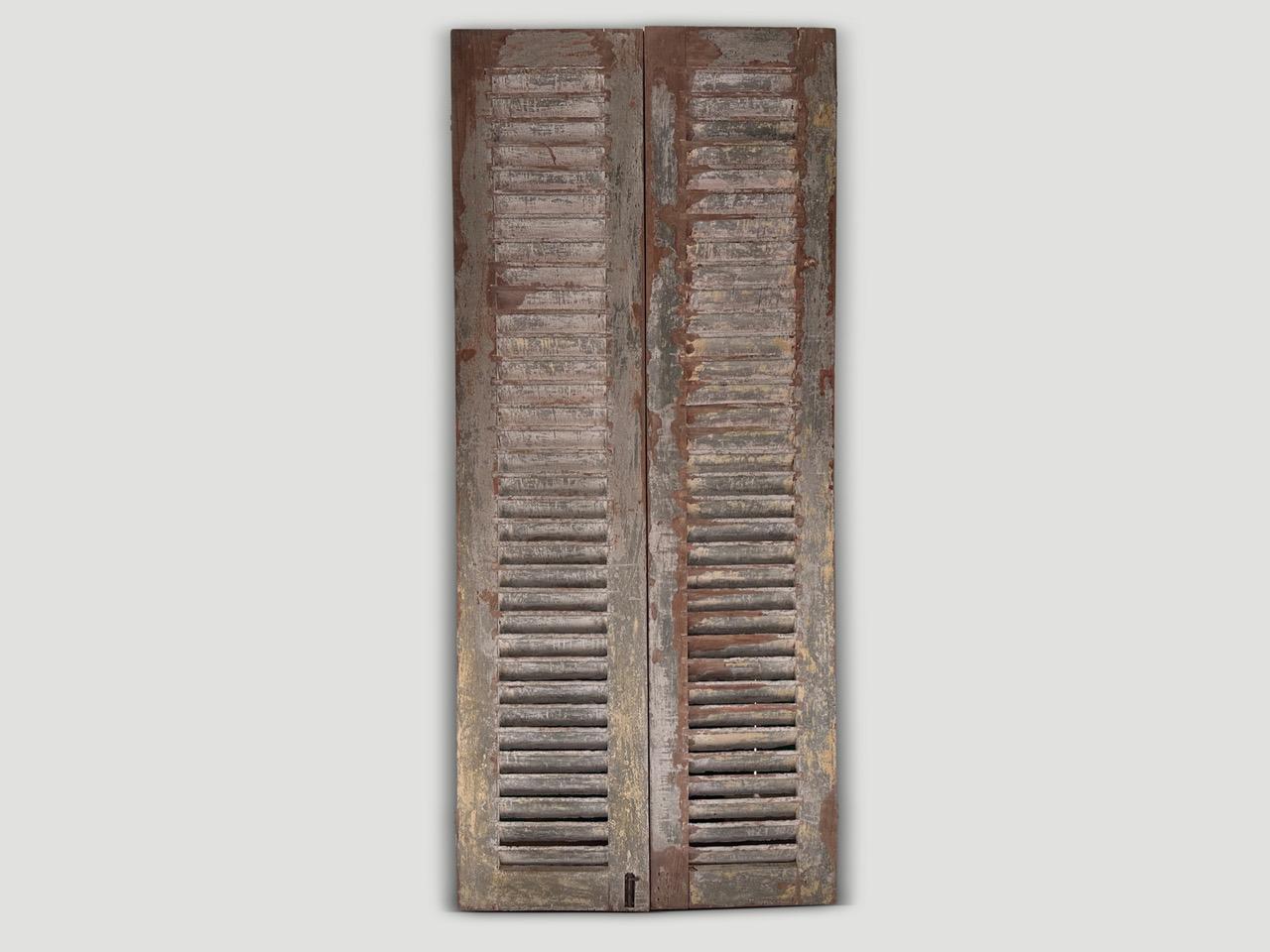 Stunningly beautiful antique shutters with the remnants of the original color, over the natural aged teak wood. Circa 1940. Full dimensions; 100” high x 44” wide x 1.5 thick frame, plus bevel at 3” total thickness.

A set of beautiful shutters hand