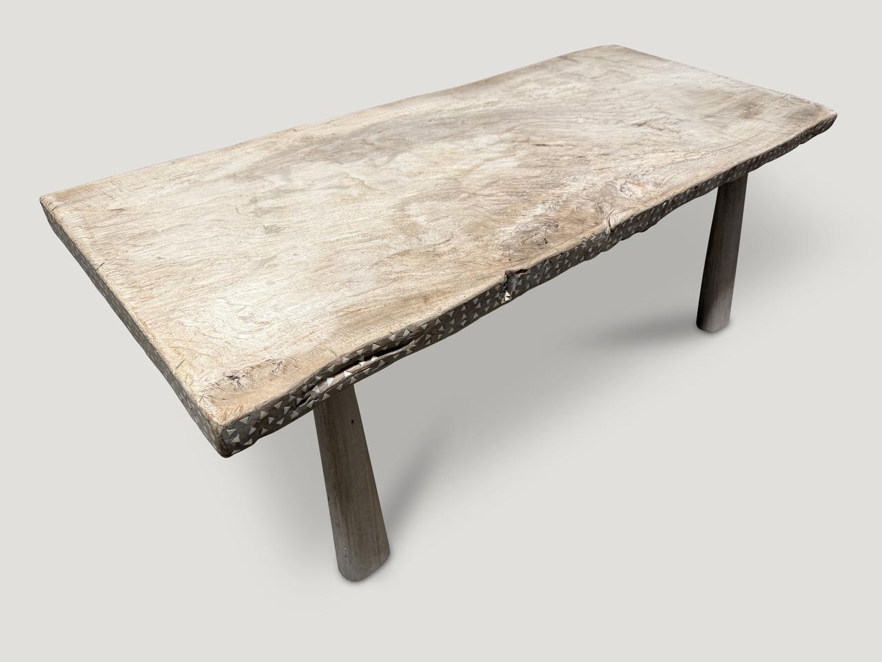 A beautiful century old two inch thick teak slab with a slight live edge, has been hand crafted into a unique coffee table whilst respecting the natural organic wood. The top is supported with minimalist hand carved legs. We added shell inlay into