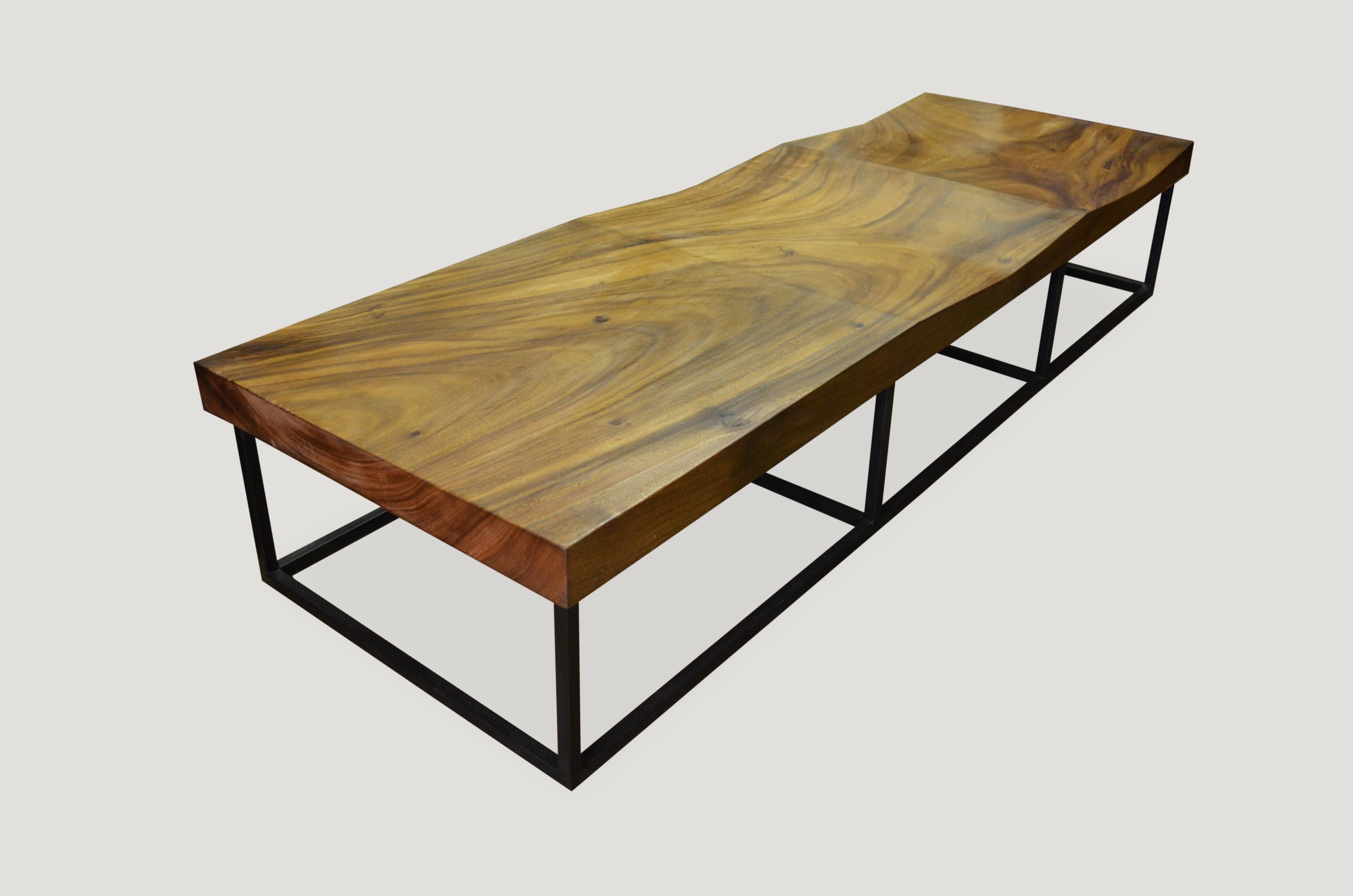A single 3” thick slab of reclaimed suar wood, with a beautiful wood grain color tone. Set on a modern metal base. There is a soft hand carved wave for seating and a 25.5” long flat section which can be used as seating or for a side table/coffee