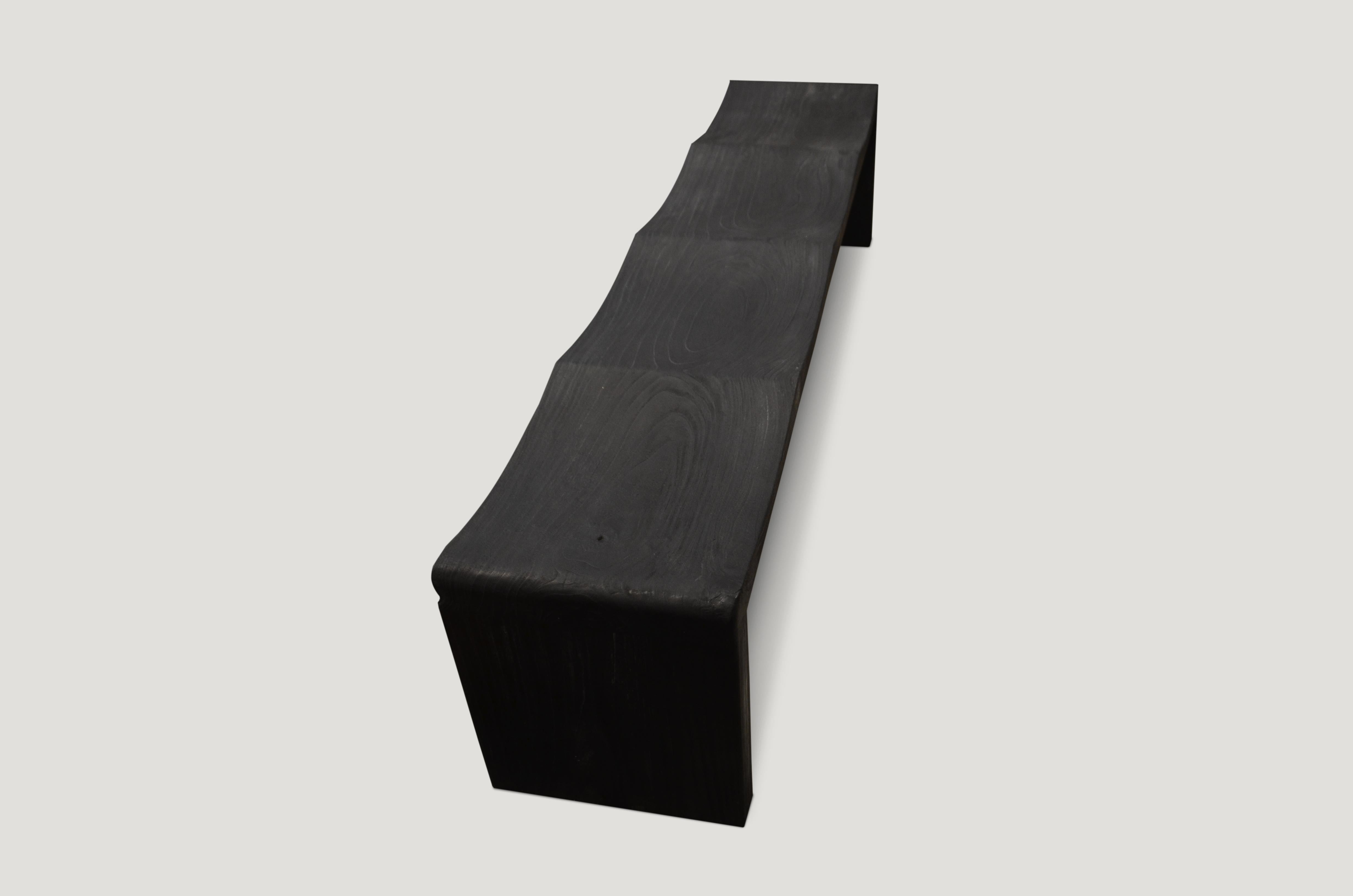 The teak wave bench represents a sleek, modern aesthetic, designed to provide comfort and durability. Solid reclaimed teak wood is hand carved into a wave design. Burnt, sanded and sealed leaving the grain of the wood showing. Available in matte and