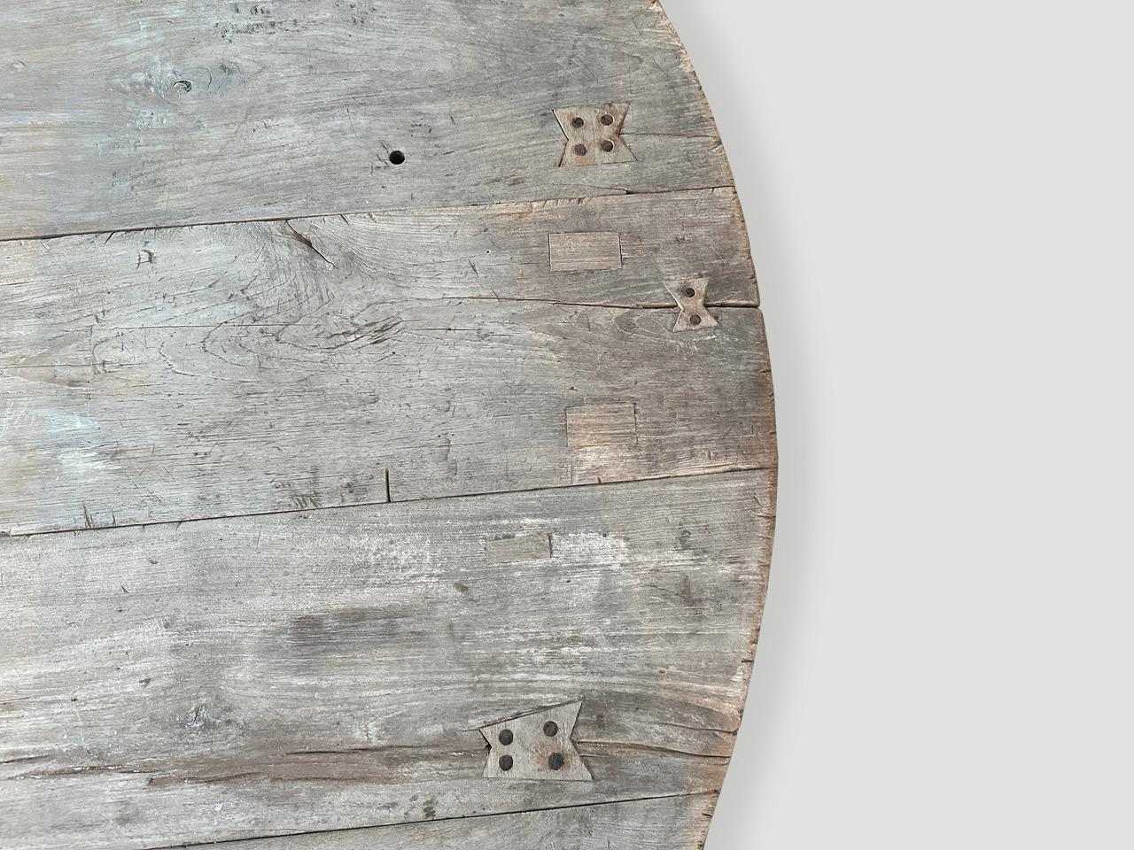 De magnifiques panneaux de bois de teck ancien, joliment patinés et aux bords arrondis, sont assemblés pour produire cette fabuleuse table basse ronde. Nous avons ajouté des papillons incrustés dans le bois et une base lisse en teck de style mid