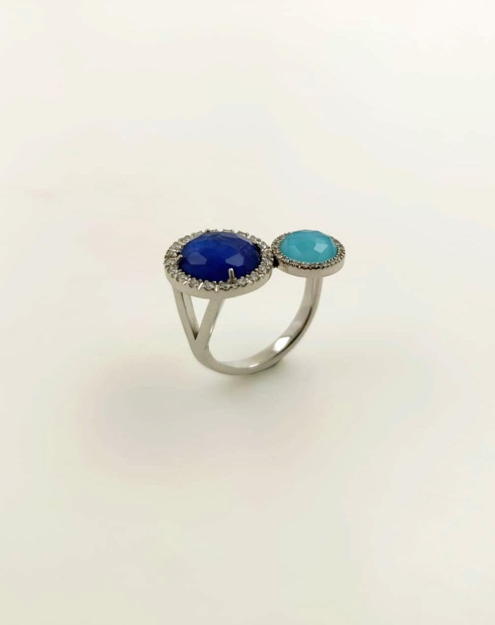 Anello in oro bianco 18k con diamanti naturali taglio brillante, qualità G/VVS. 
Il design presenta due triplette con taglio briolette:
una composta da zaffiro blu e cristallo di rocca, l'altra da turchese e cristallo di rocca.
Le pietre sono