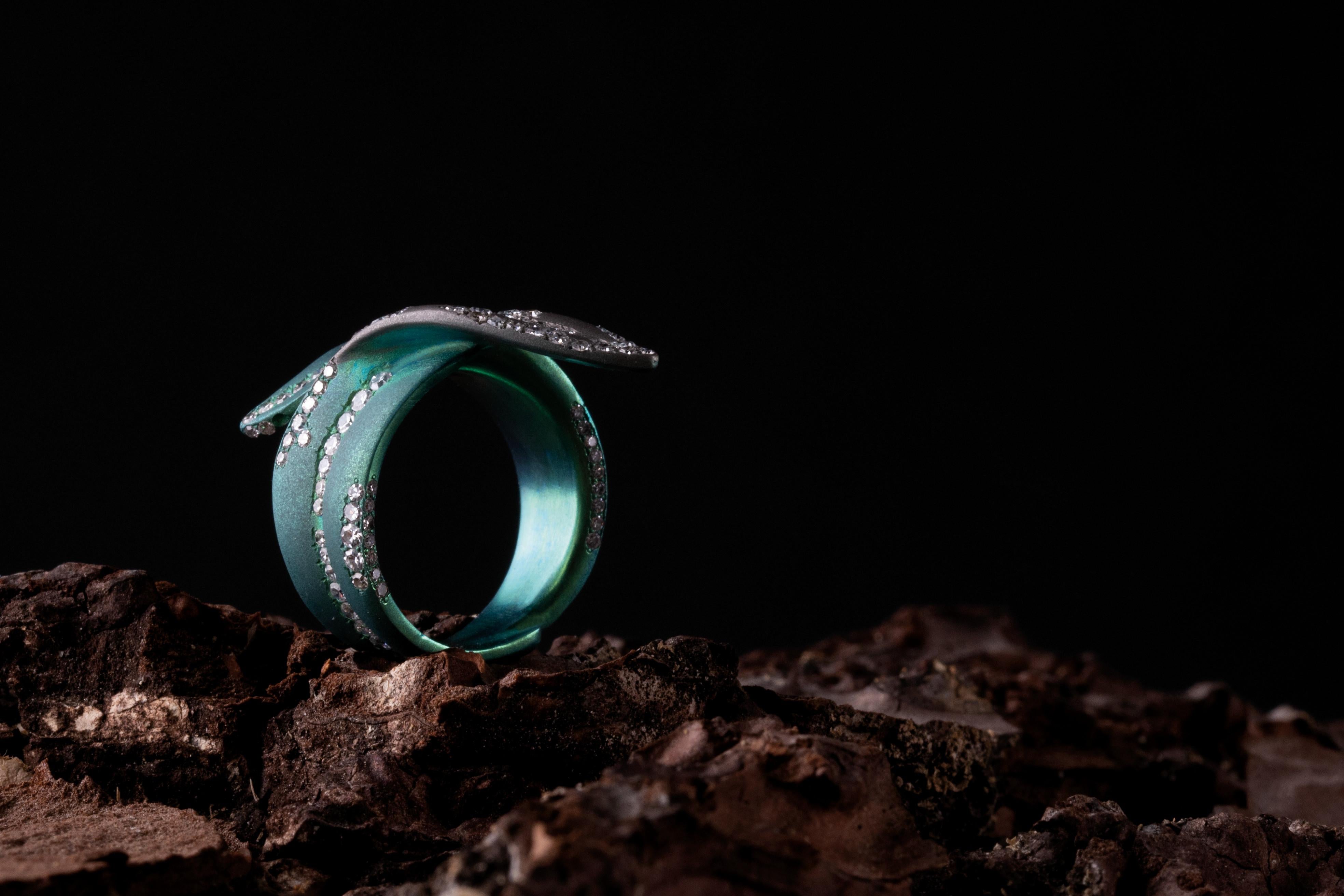 Anello realizzato in titanio in parte anodizzato verde, impreziosito da piccoli diamanti rotondi taglio semplice peso carati 1,23. 
È un pezzo unico. 
La leggerezza del materiale rende molto confortevole la vestibilità dell'anello. 
Il colore verde