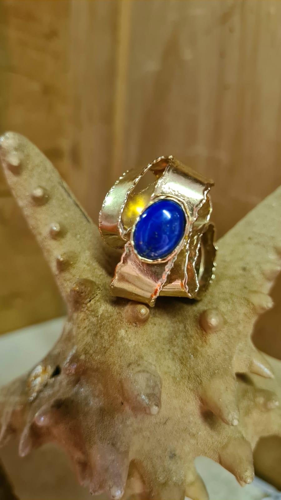 Un anello-scultura Onda con Lapislazzuli che cattura il movimento fluido dell'acqua attraverso le sue curve ondulate. Réalisé à la main en argent 925 et plaqué en or 24 carats, ce bijou se distingue par sa structure organique et matérielle,