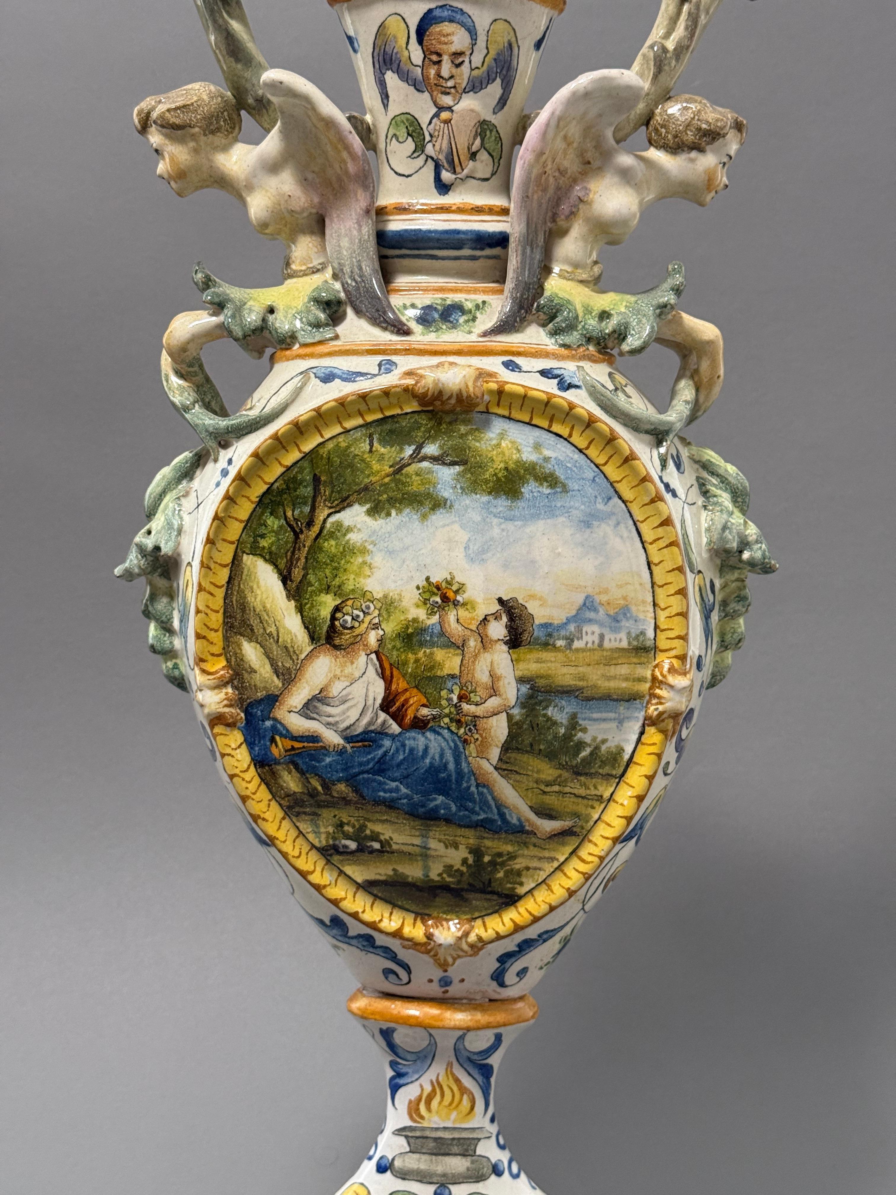 Anfora in ceramica biansata maiolicata della seconda metà del 1800, di manifattura napoletana. Presenta uno stile classico con decorazioni mitologiche da un lato e, grottesche dall'altro, che richiamano uno stile prettamente cinquecentesco. I manici