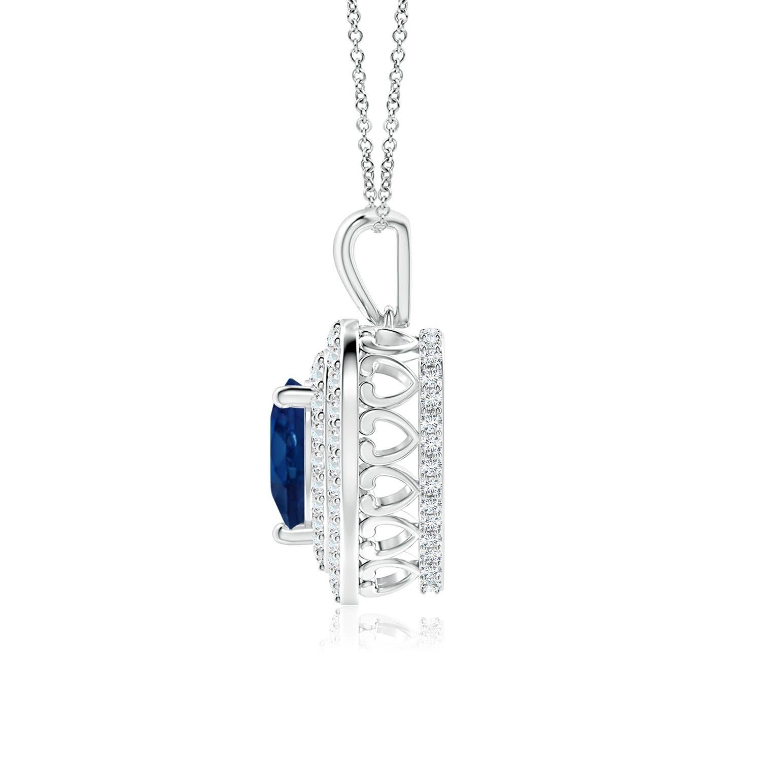 Un saphir bleu en forme de cœur est entouré d'un double halo serti de diamants rayonnants dans un serti clos. Un motif en forme de cœur incrusté de diamants relie la balle en métal au cadre en forme de cœur. Les diamants étincelants créent un