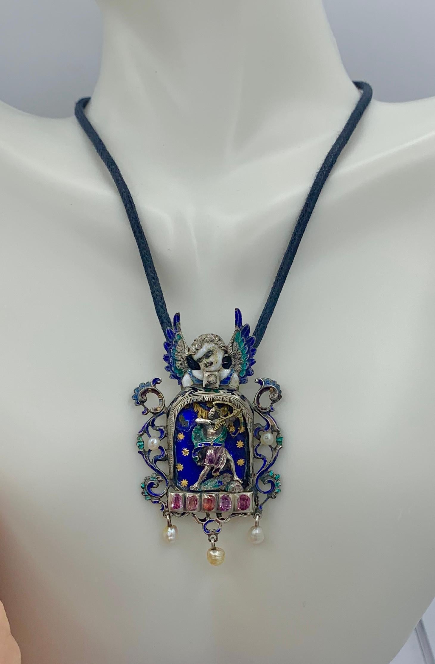 Il s'agit d'un magnifique collier pendentif austro-hongrois en rubis, diamant, émail et perle, de qualité musée, représentant un Cupidon archer avec son arc et sa flèche, avec un fabuleux ange ailé au sommet.  Le pendentif est de style