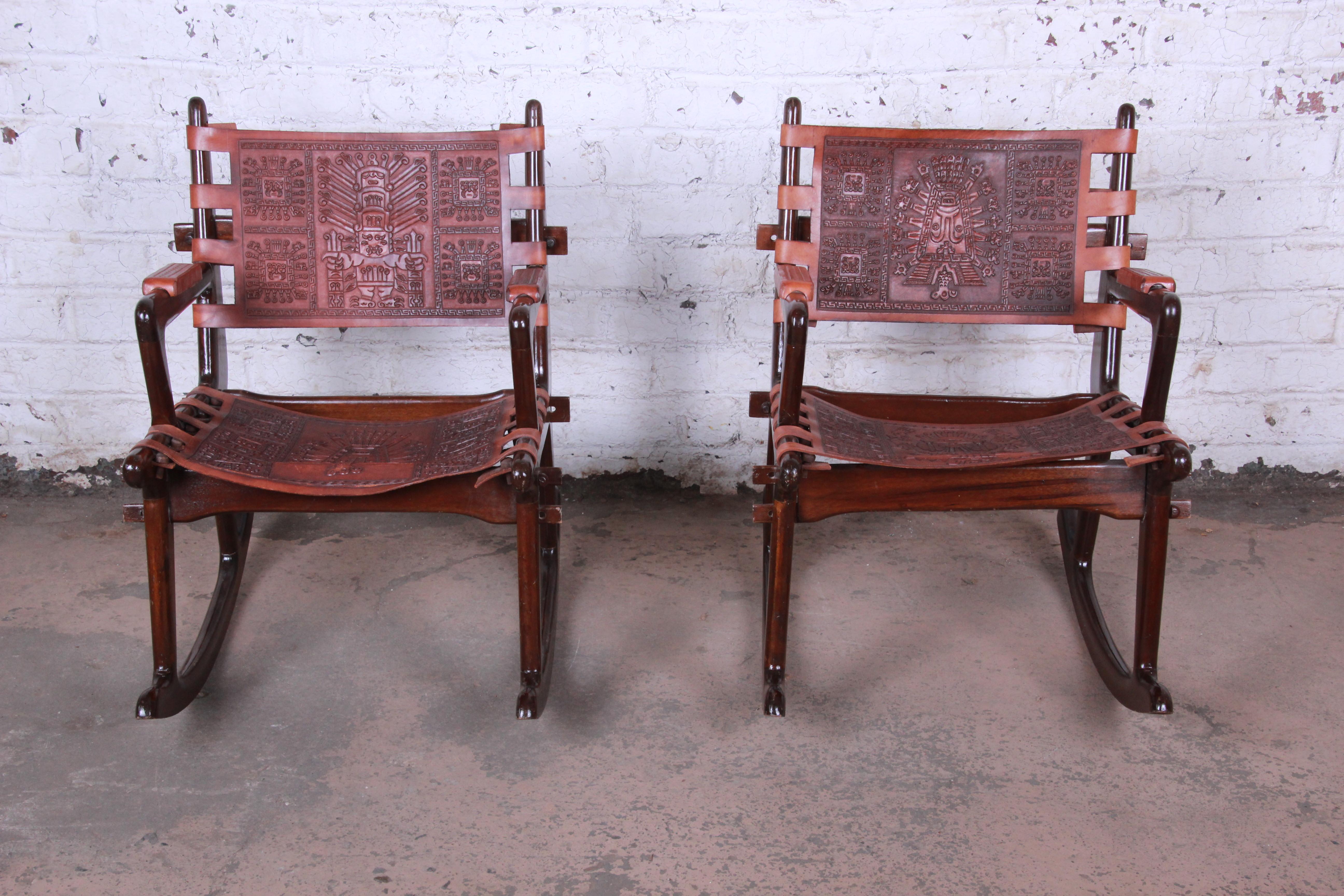 A gorgeous pair of Ecuadorian wood and saddle brown leather rocking chairs by Angel Pazmino for Muebles de Estillo. The chairs feature solid teak wood construction and original heavy cowhide with unique Mayan embossed designs to the seats and