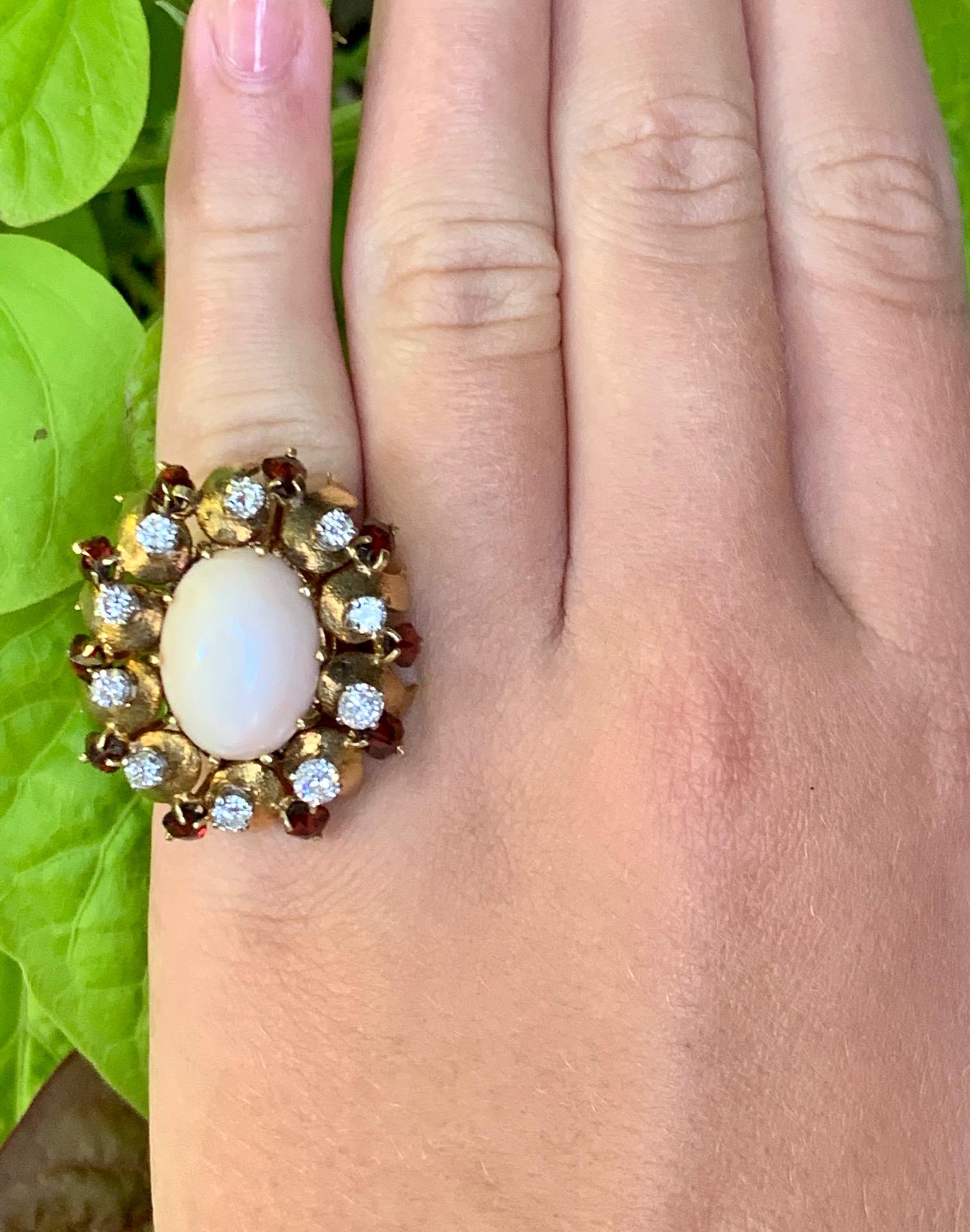 This ring features a beautiful Angel Skin Coral cabochon as the center stone.  The Coral measures 17 x 11mm.  It is surrounded by  10 pear cut 5x3mm Brown Garnets and 10 brilliant cut Diamonds. The Diamonds total approximately 1.30ctw with an