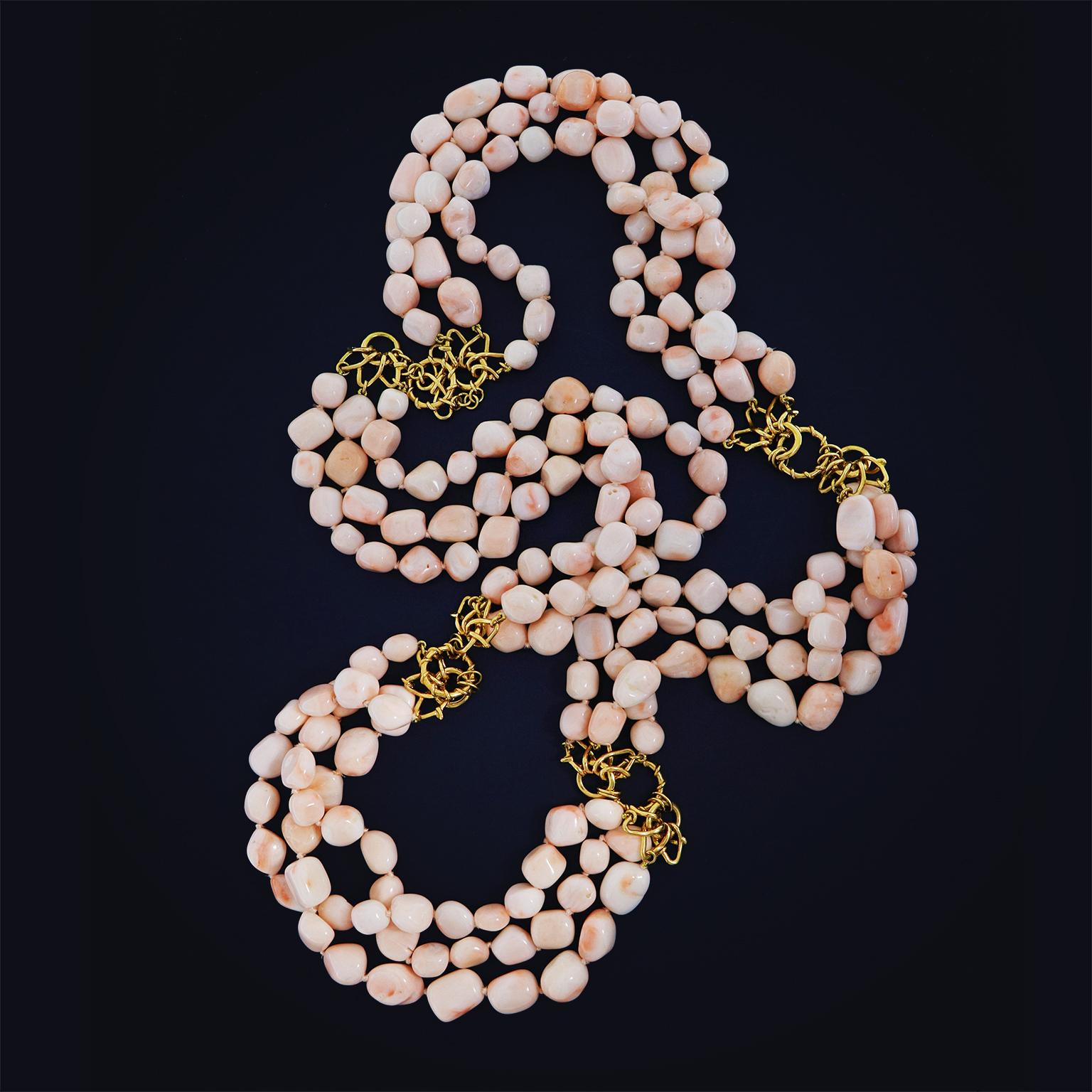 The soft hue of angel skin coral is elevated by carved nuggets on three strands. 18k yellow gold Vs in connected to gold rings in three sets disperse throughout the necklace to connect the coral strands. The total weight of the corals is 230 carats.