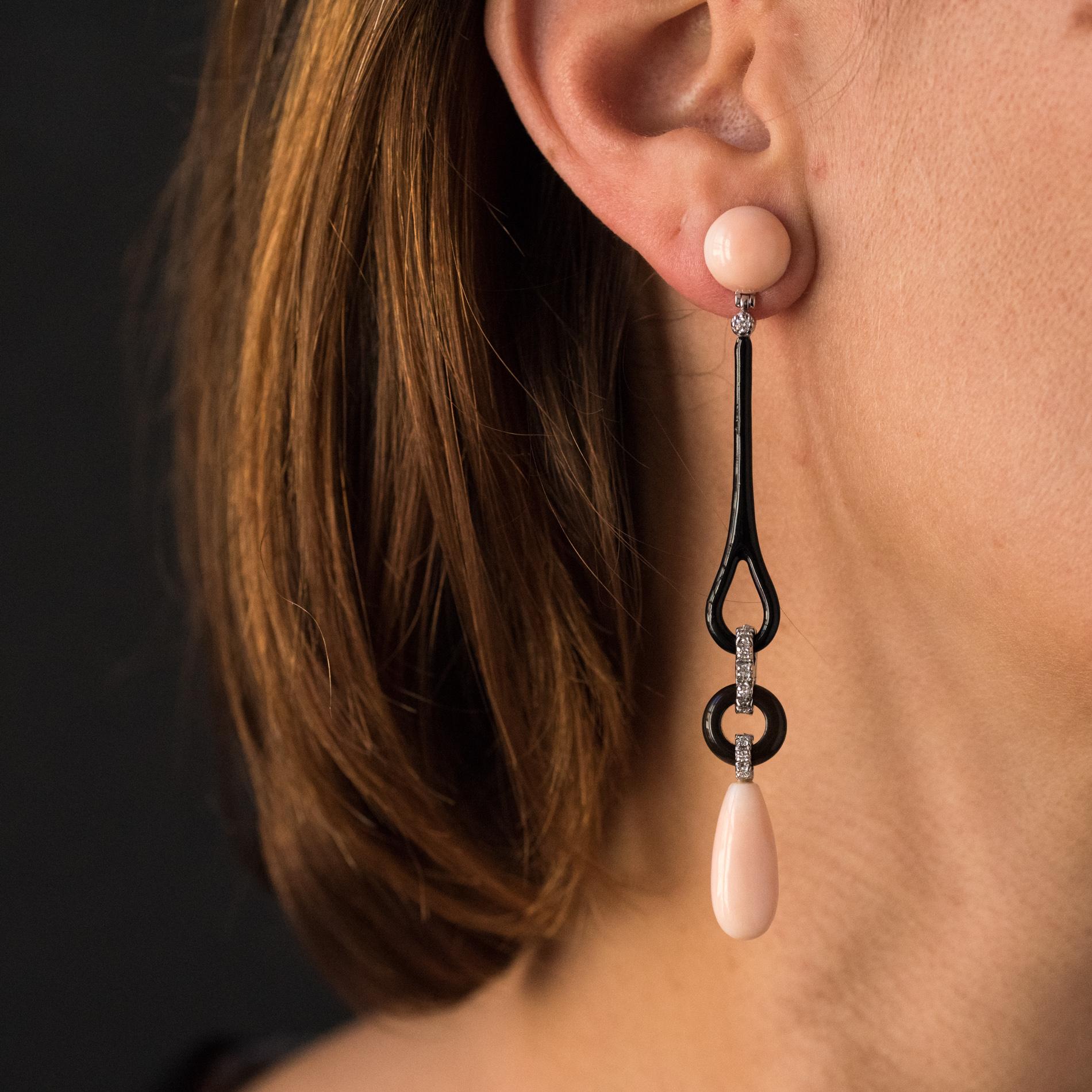 For pierced ears.
Earrings in 18 karats white gold.
Long dangle earrings, they consist of a pink angel skin coral cabochon that retains a long pattern of black enamel, topped with a diamond. At its base, a knot set with diamonds retains a disc of