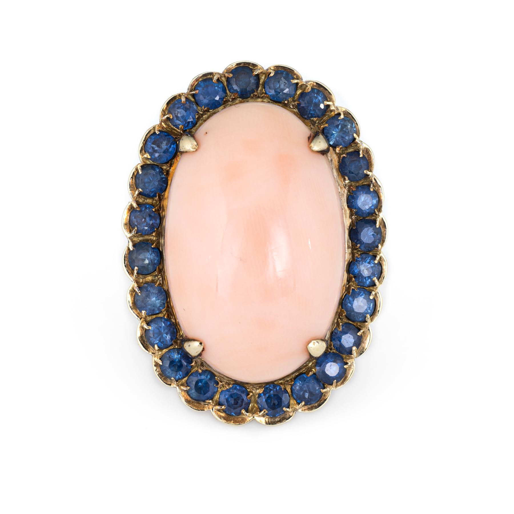 Finely detailed vintage angel skin coral & sapphire cocktail ring (circa1950s to 1960s), crafted in 14 karat yellow gold. 

Cabochon cut angel skin coral measures 21mm x 13.5mm (estimated at 20 carats), accented with 25 estimated 0.05 carat blue